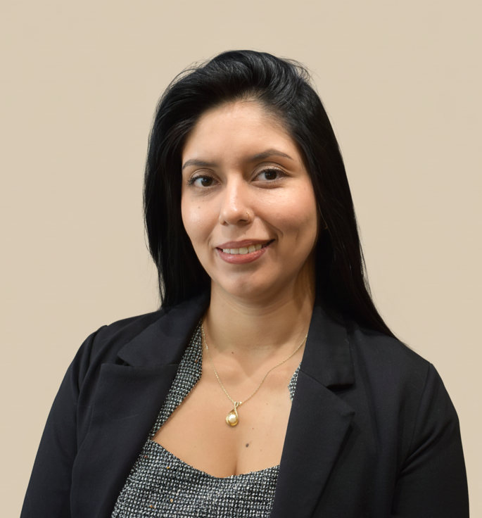 A woman with long black hair, wearing a black blazer and a patterned top, smiling at the camera against a beige background.