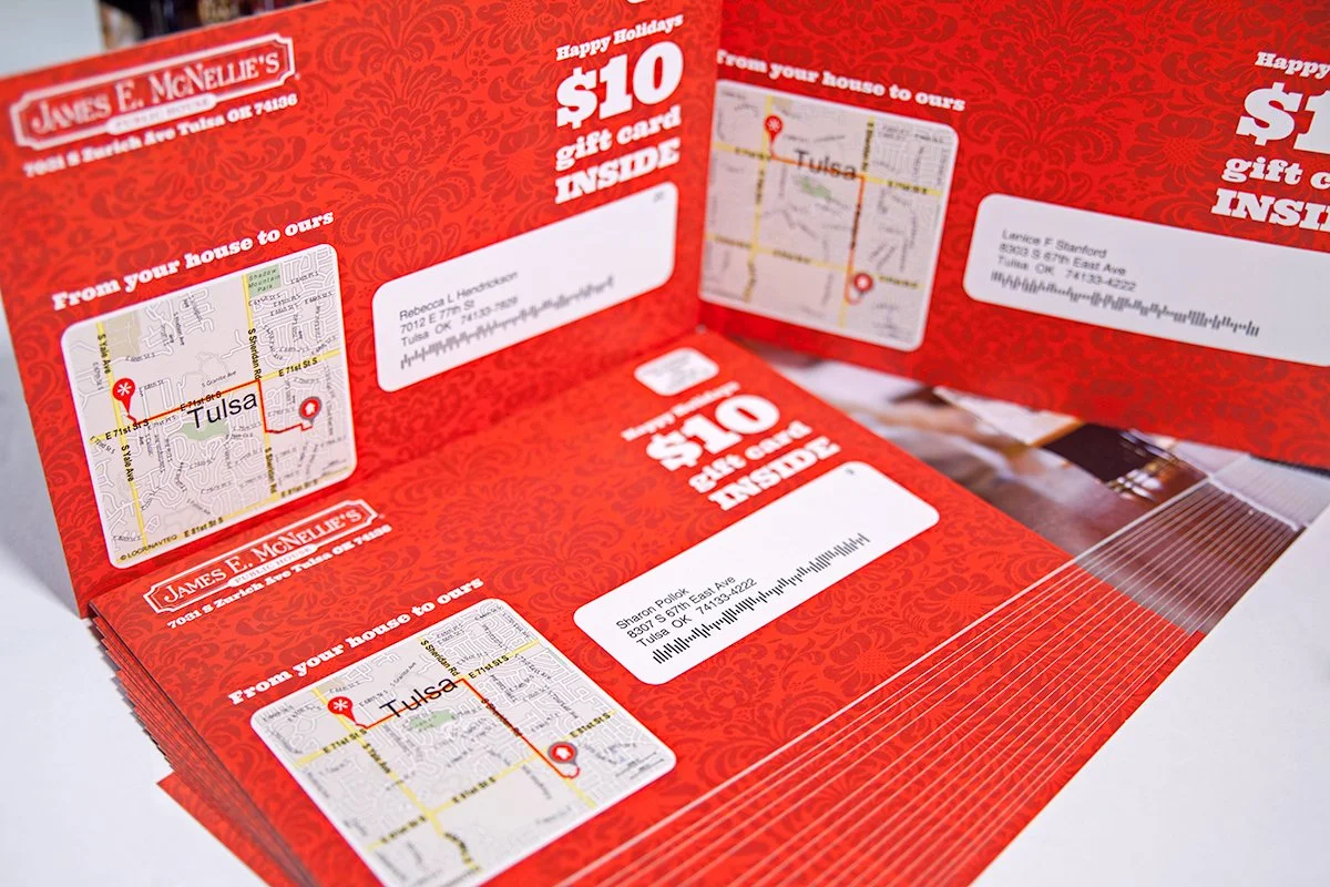 A folded promotional flyer with a red patterned background offering $10 gift cards inside, promoting local businesses in Tulsa, Oklahoma, with maps and addresses.