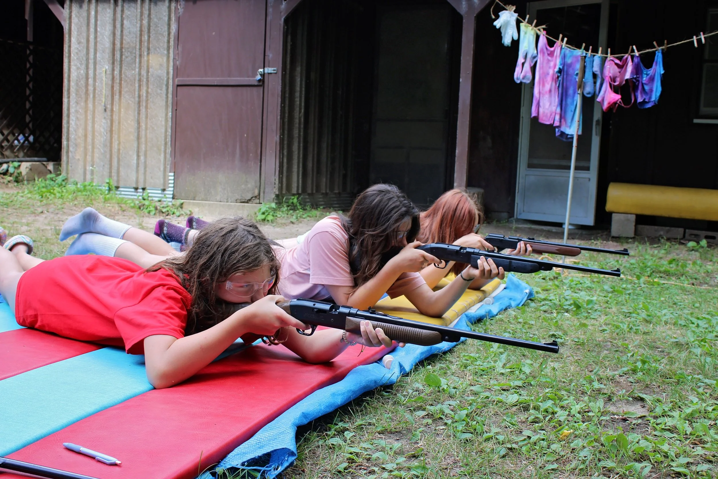 Three girls shooting in prone position on mat in marksmanship