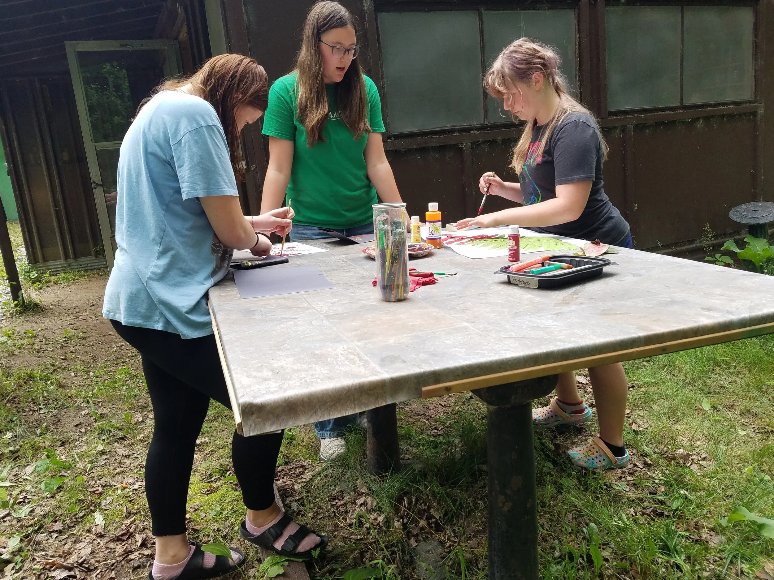Three girls painting on outside crafts table