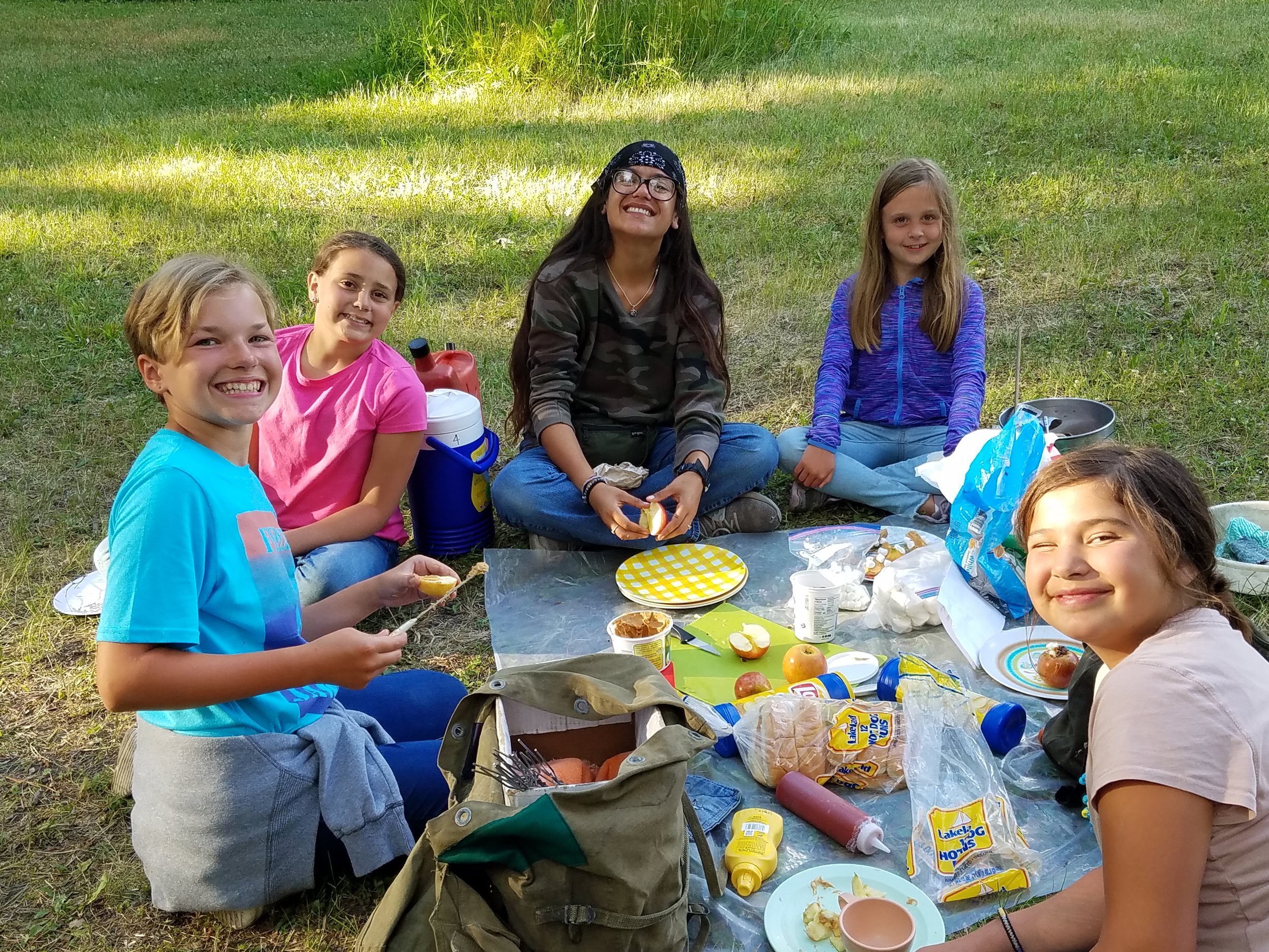 Girls preparing food on tarp at cookout