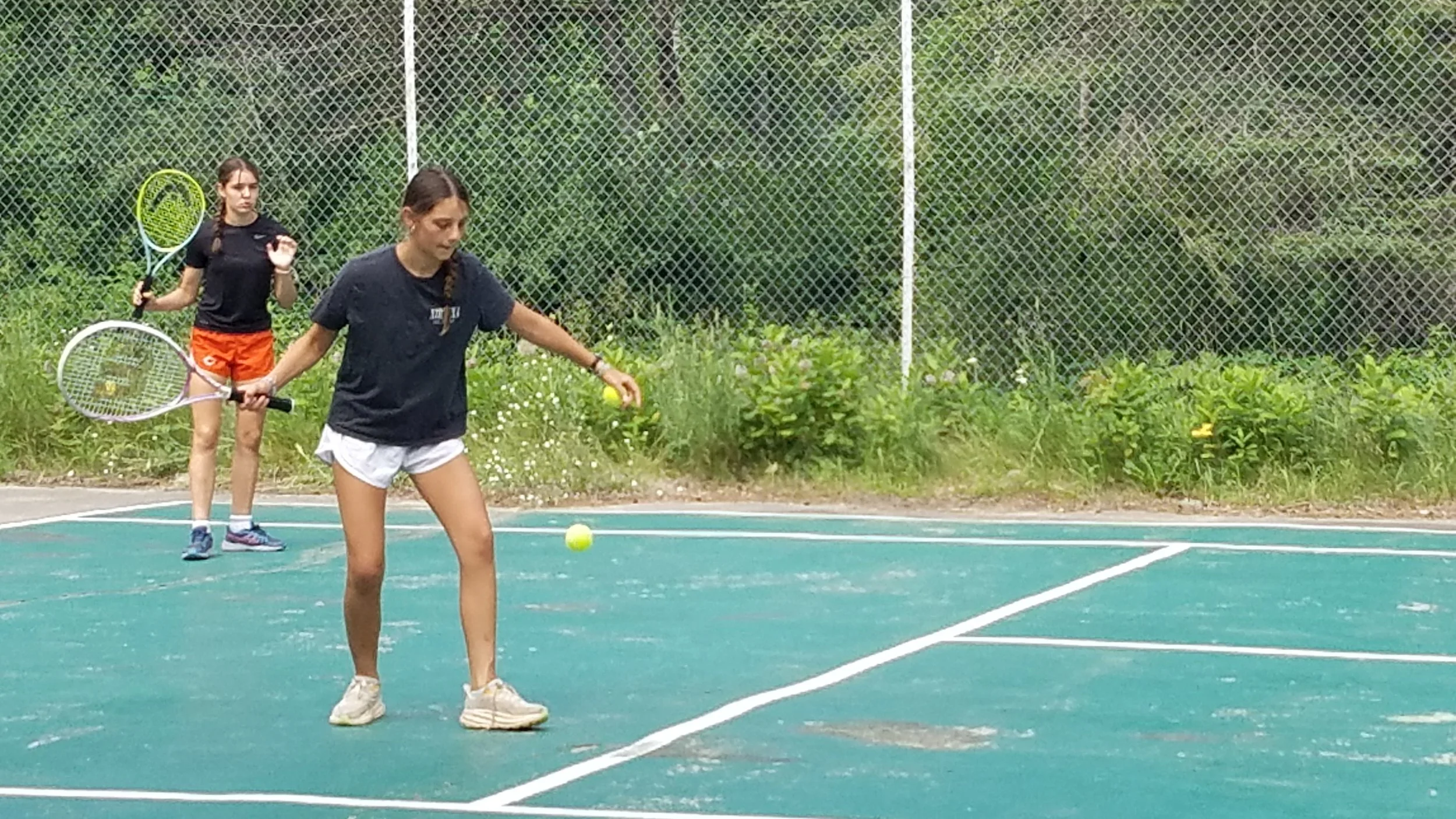 Two girls on tennis court, one hitting a tennis ball