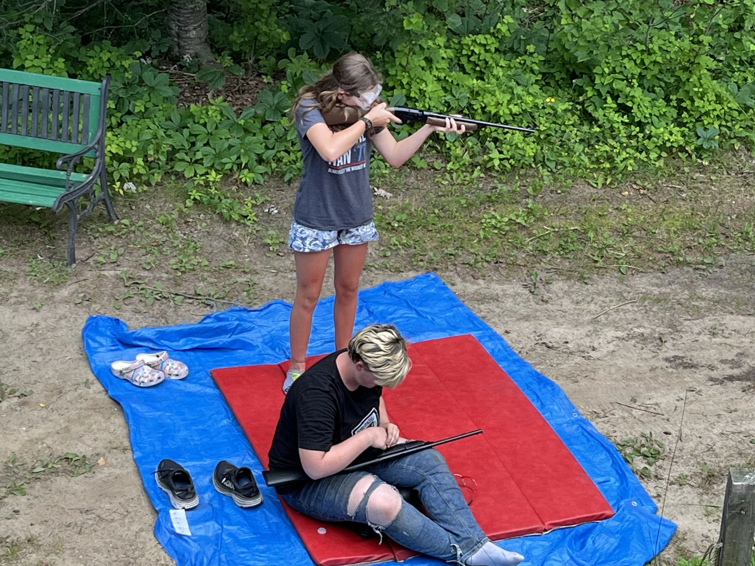 Two girls, standing and sitting, using bb guns in marksmanship