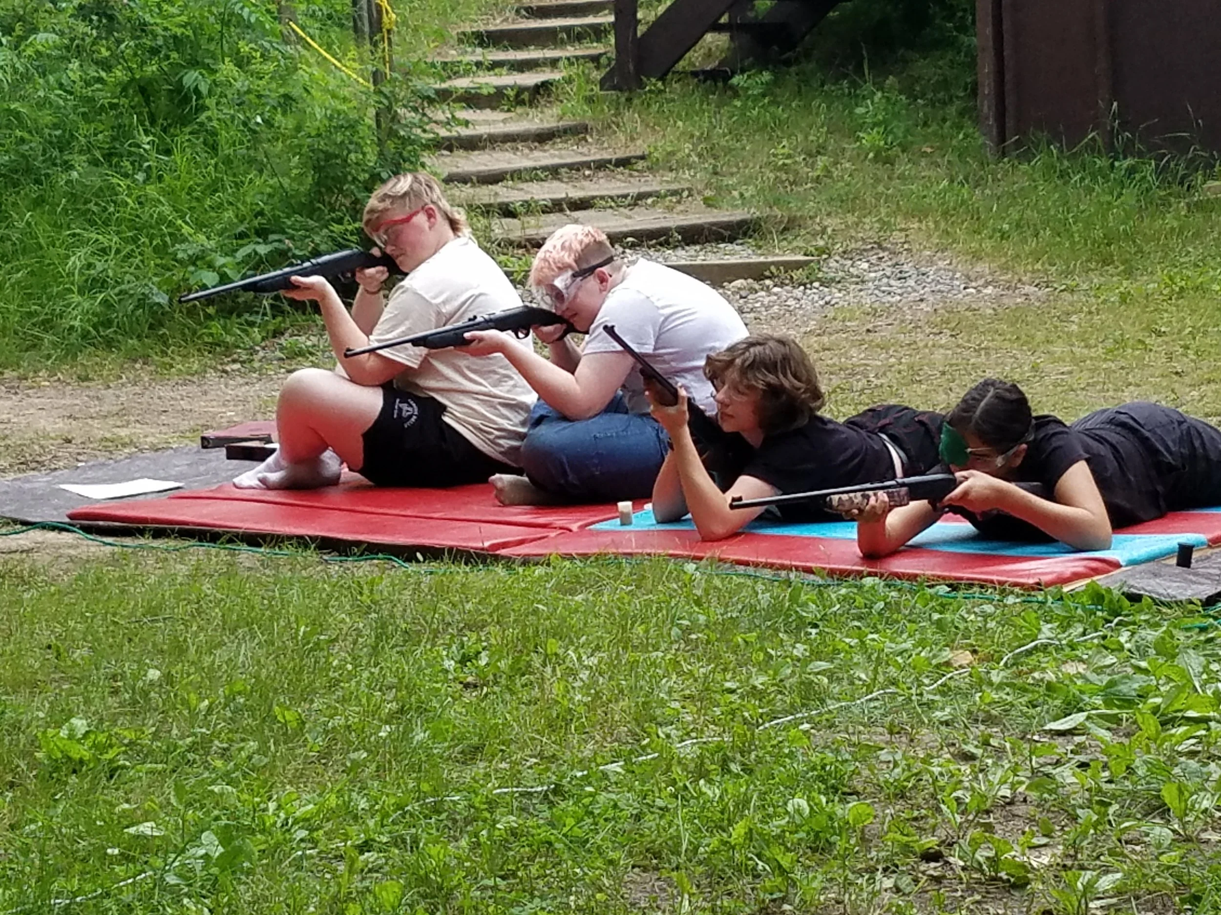 Three girls aiming bb guns, one girl preparing air gun to shoot