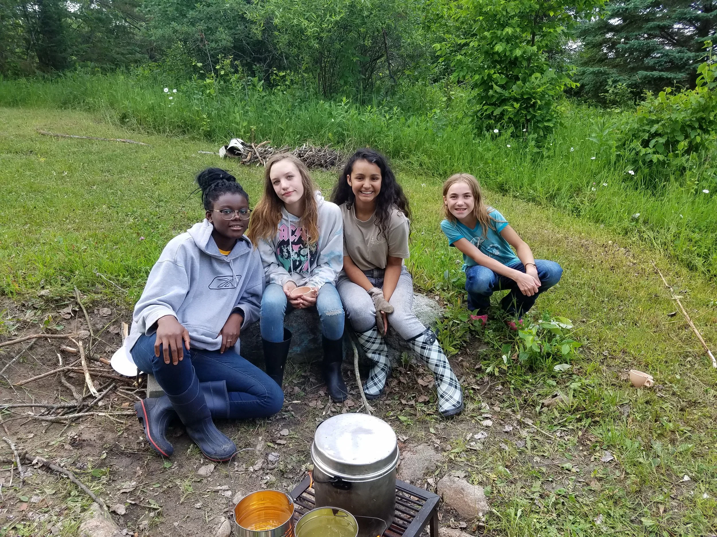 Four girls sitting by fire cooking in large pot