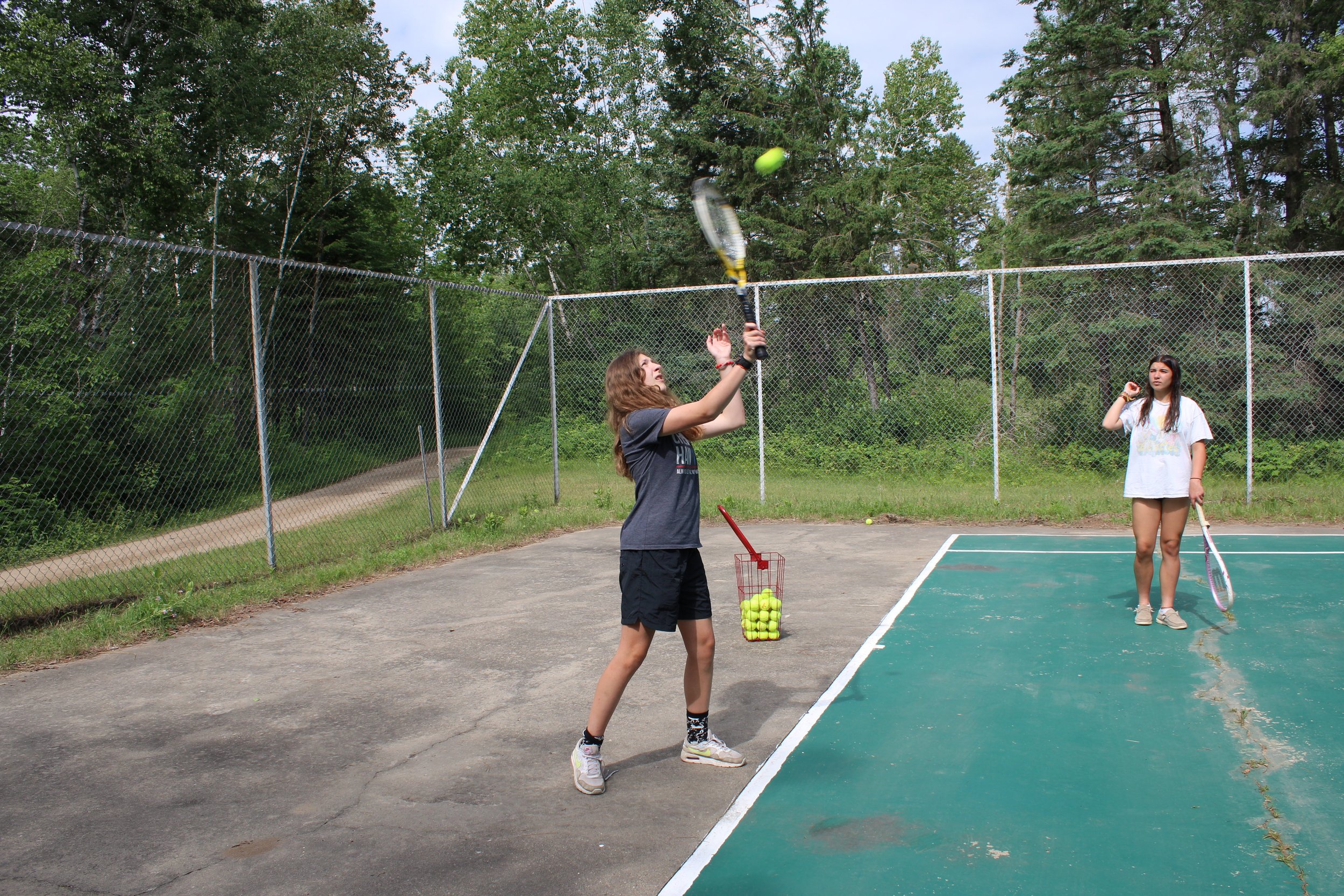 Two girls playing tennis, one serving ball