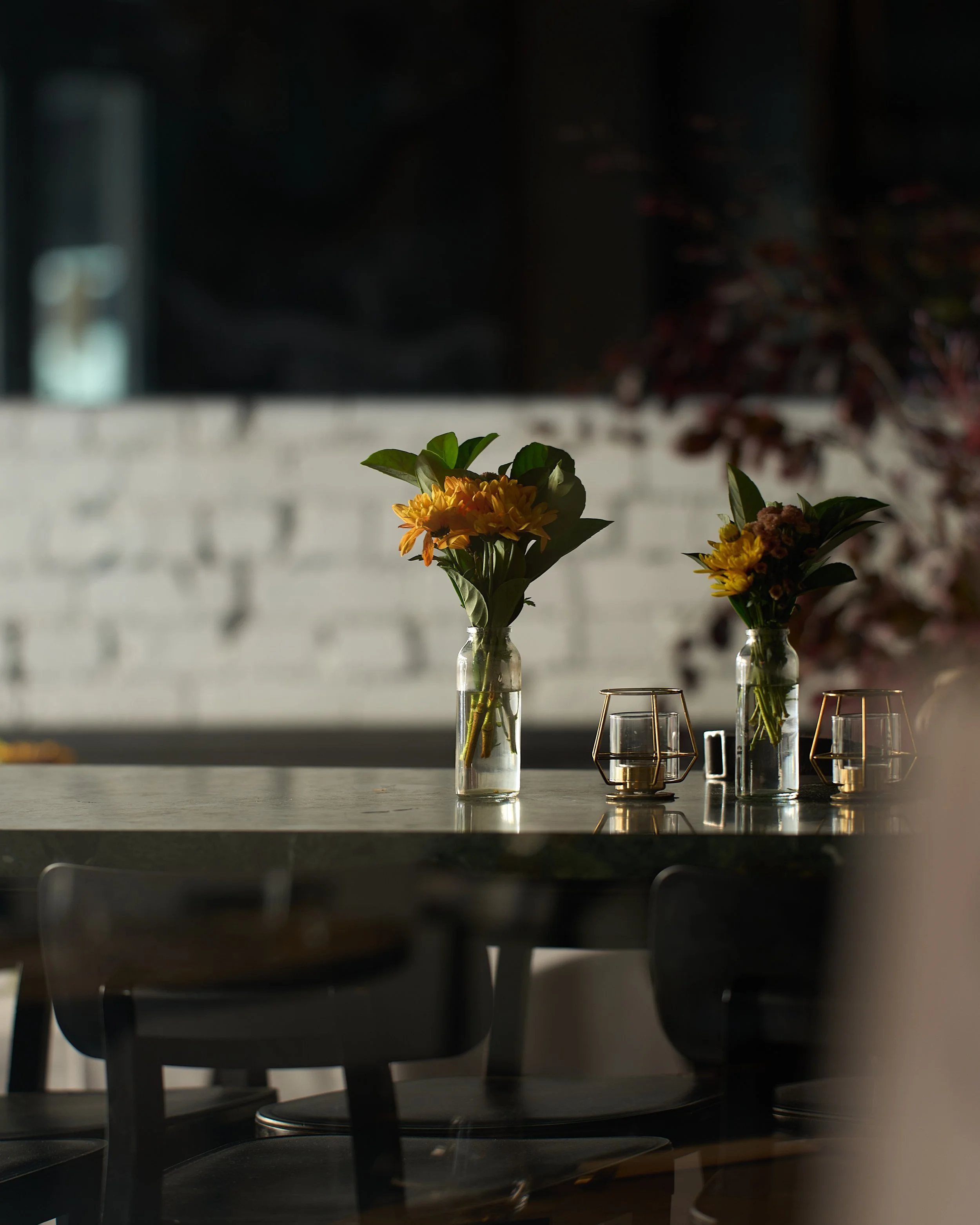 Two small vases with flowers on a table in Estelle, sunlight casting shadows.