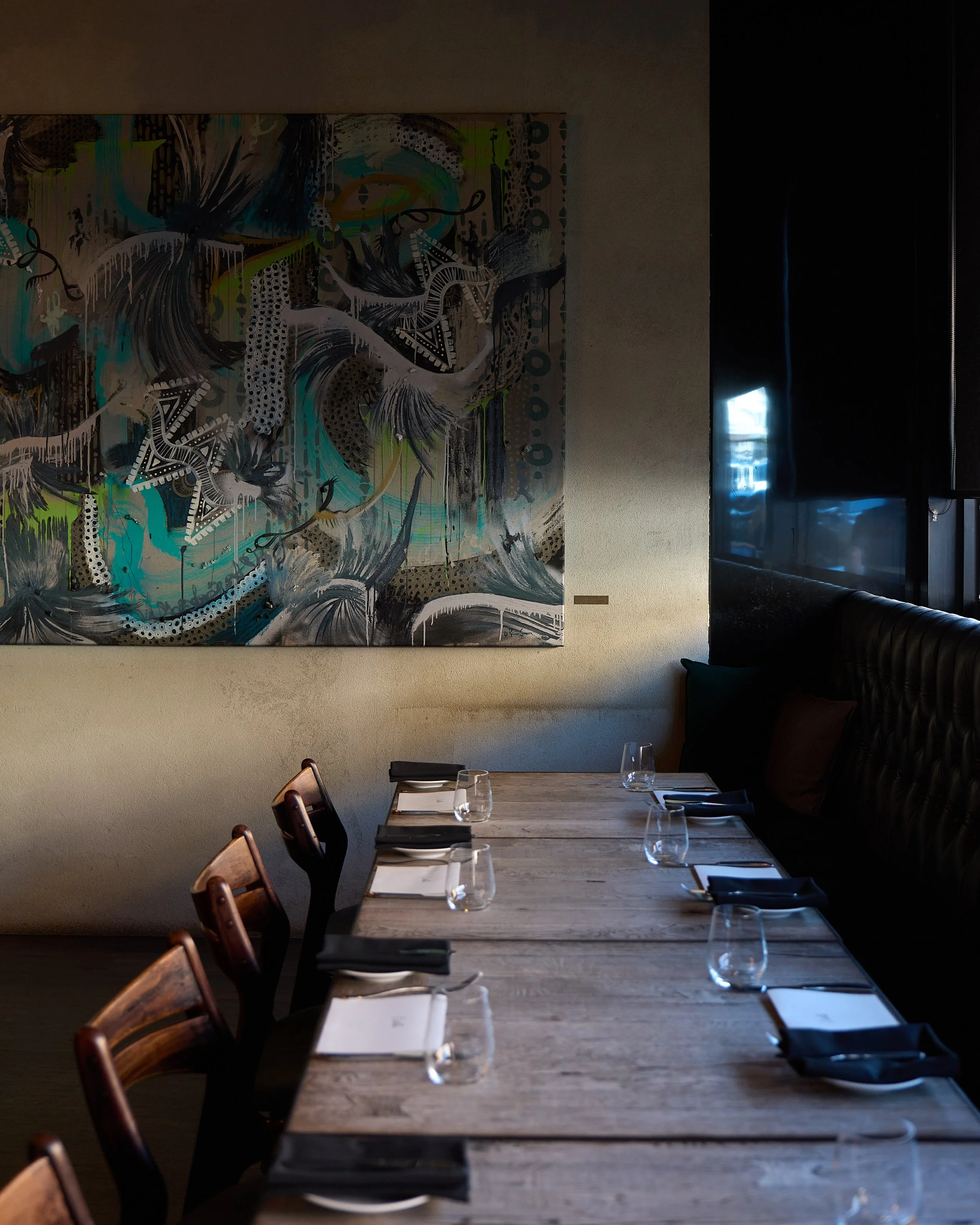 Estelle dining room table set with plates, glasses, and napkins, with a large abstract painting on the wall.