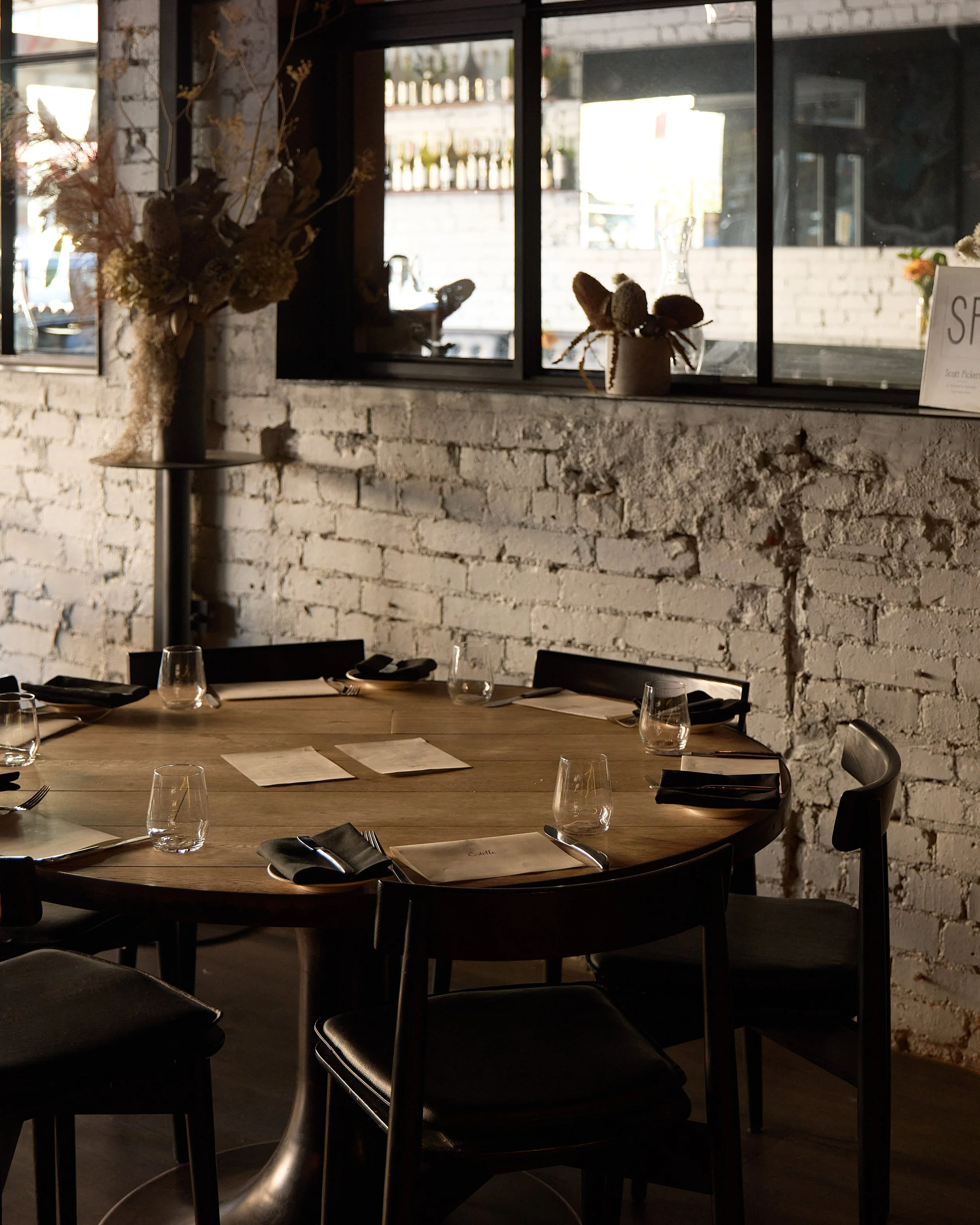 Estelle dining table set with glasses, plates, forks, and black napkins.