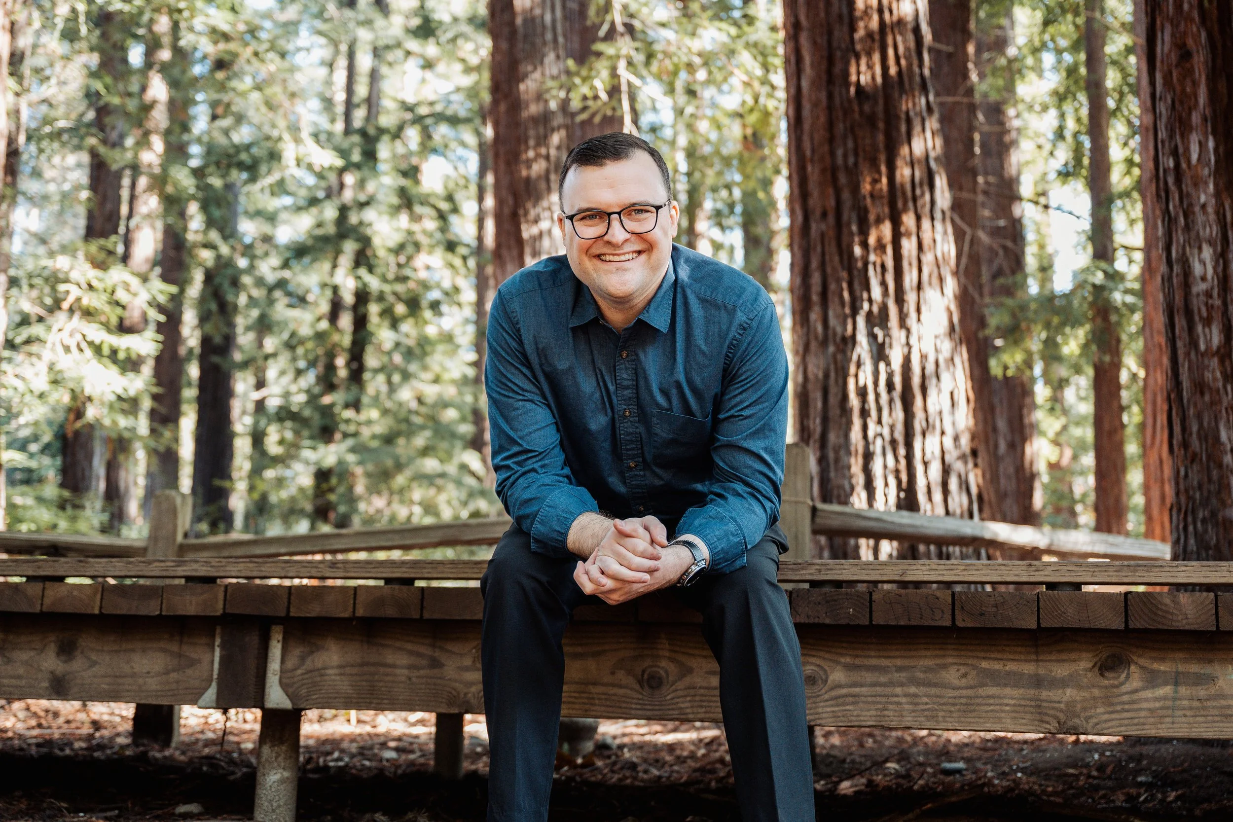 Ryan Thurwachter, LCSW smiling while sitting on a path in a redwood grove.