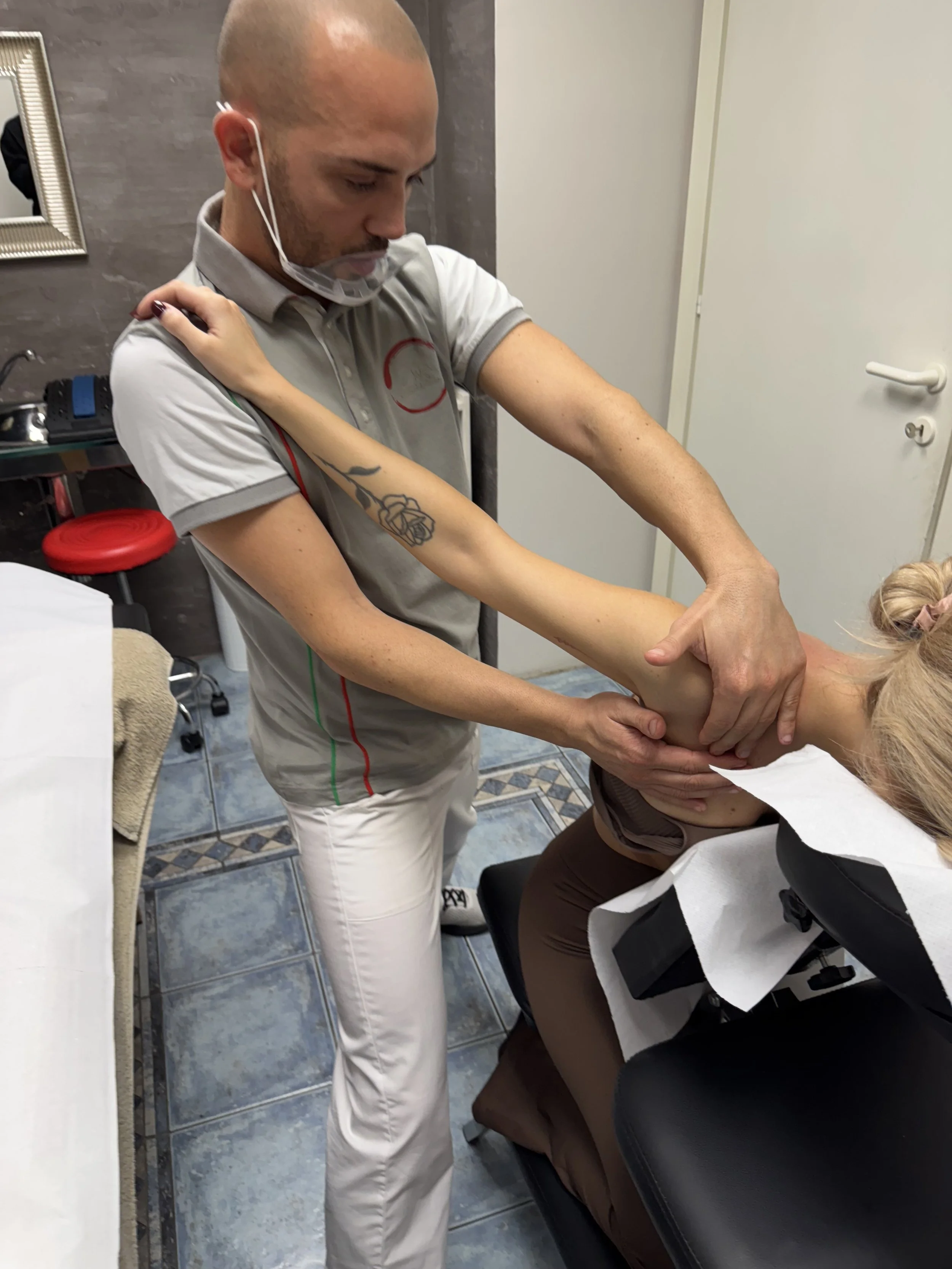 Un terapista sta facendo manipolazioni al braccio di una paziente su una sedia da trattamenti, in un ambiente clinico.