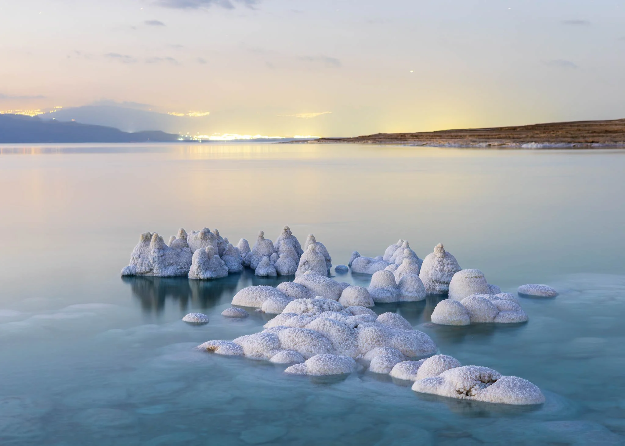 Minimalist long-exposure view of salt formations in calm Dead Sea water under a soft blue evening sky.