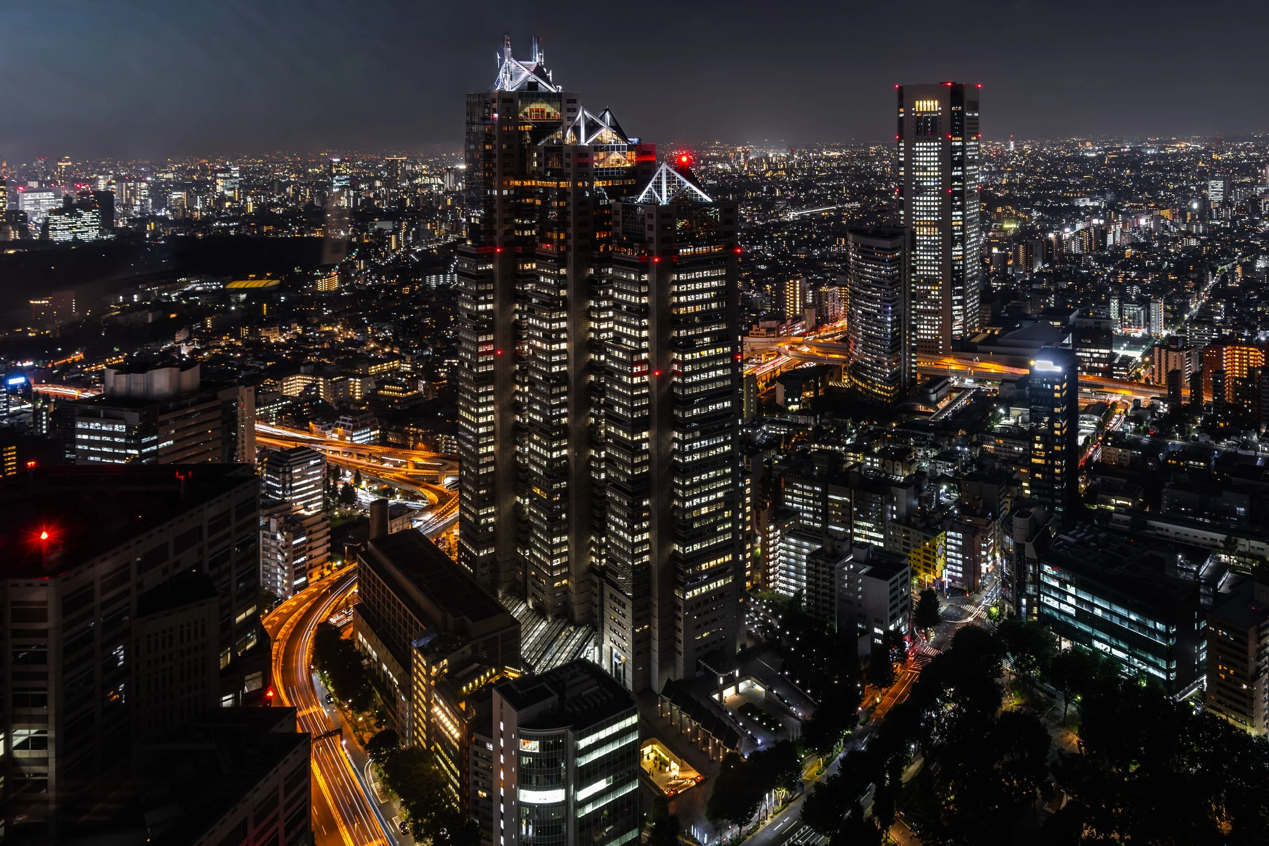 Nighttime aerial view of a city with illuminated skyscrapers and busy streets.