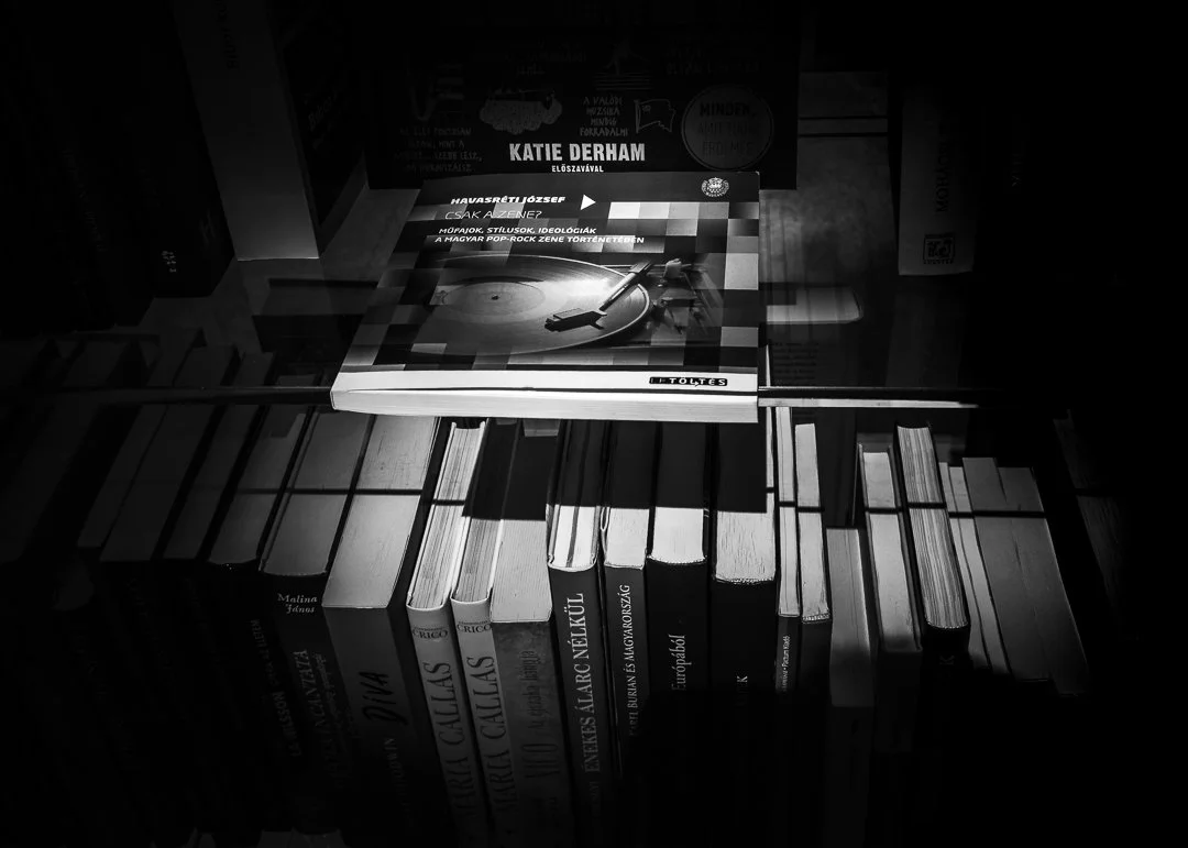 A collection of books on a bookshelf with a magazine on top of the books, featuring a vinyl record and turntable on the cover.