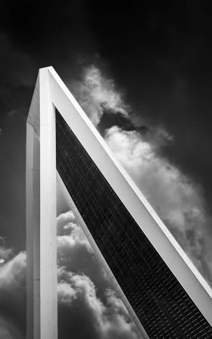 Low-angle black and white photo of the Gateway Arch against a cloudy sky.