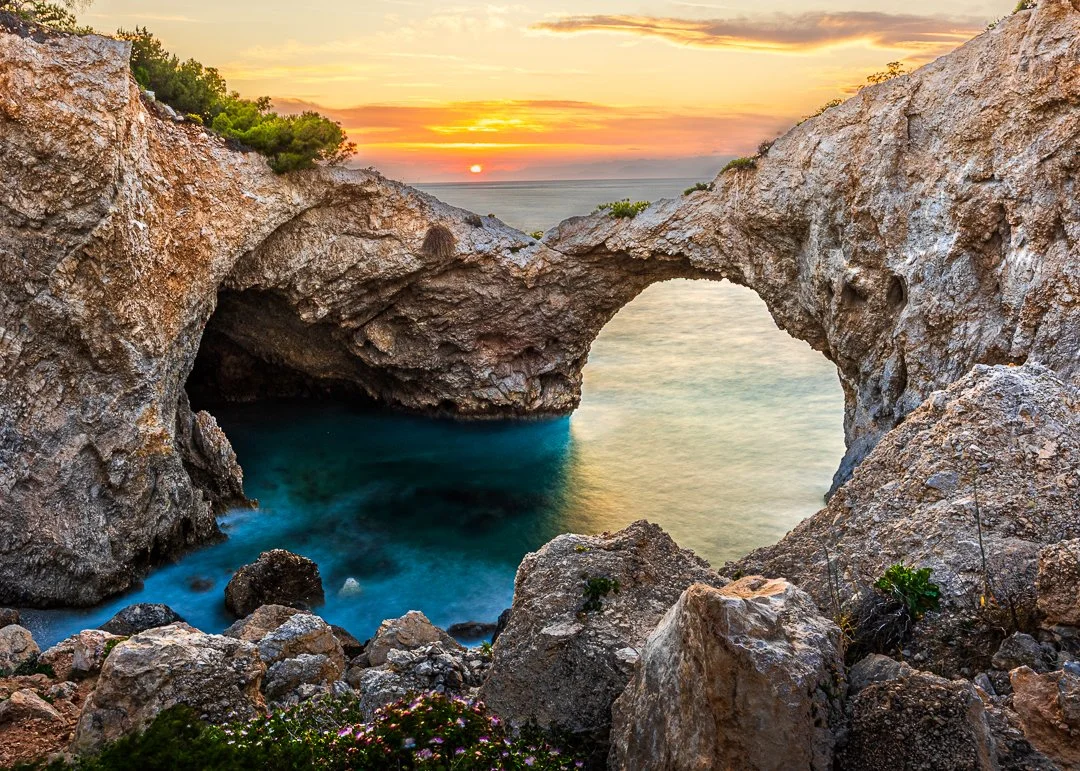 Sunset over rocky coastline with natural rock formation arch and clear water