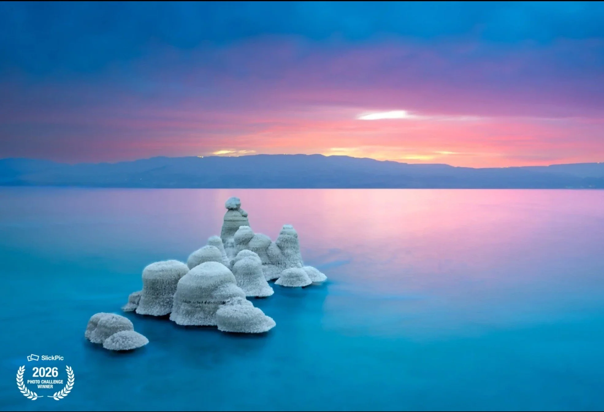 Frozen rocks in a calm body of water during sunset with pink and purple skies