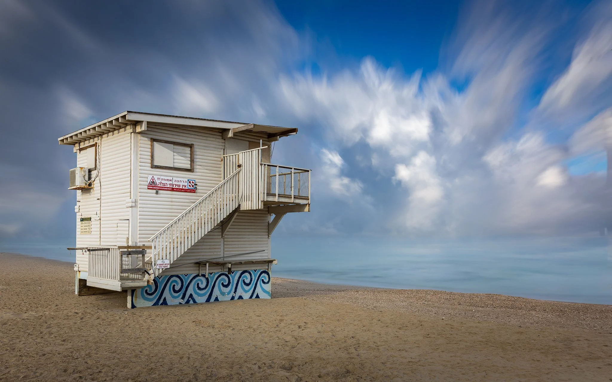 A white lifeguard tower on a sandy beach with a blue sky and clouds in the background.