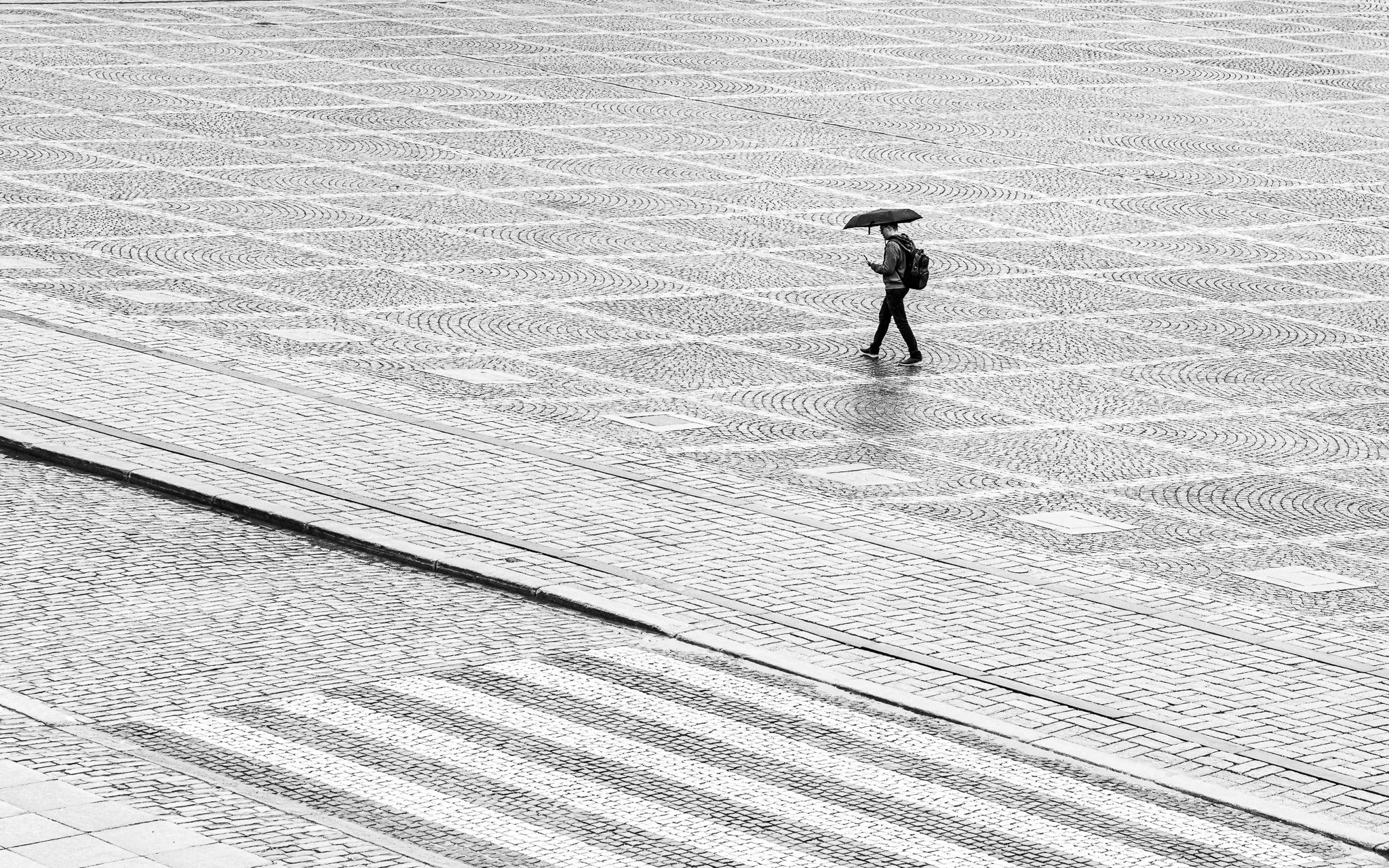 A person walking on a wet cobblestone square holding an umbrella.