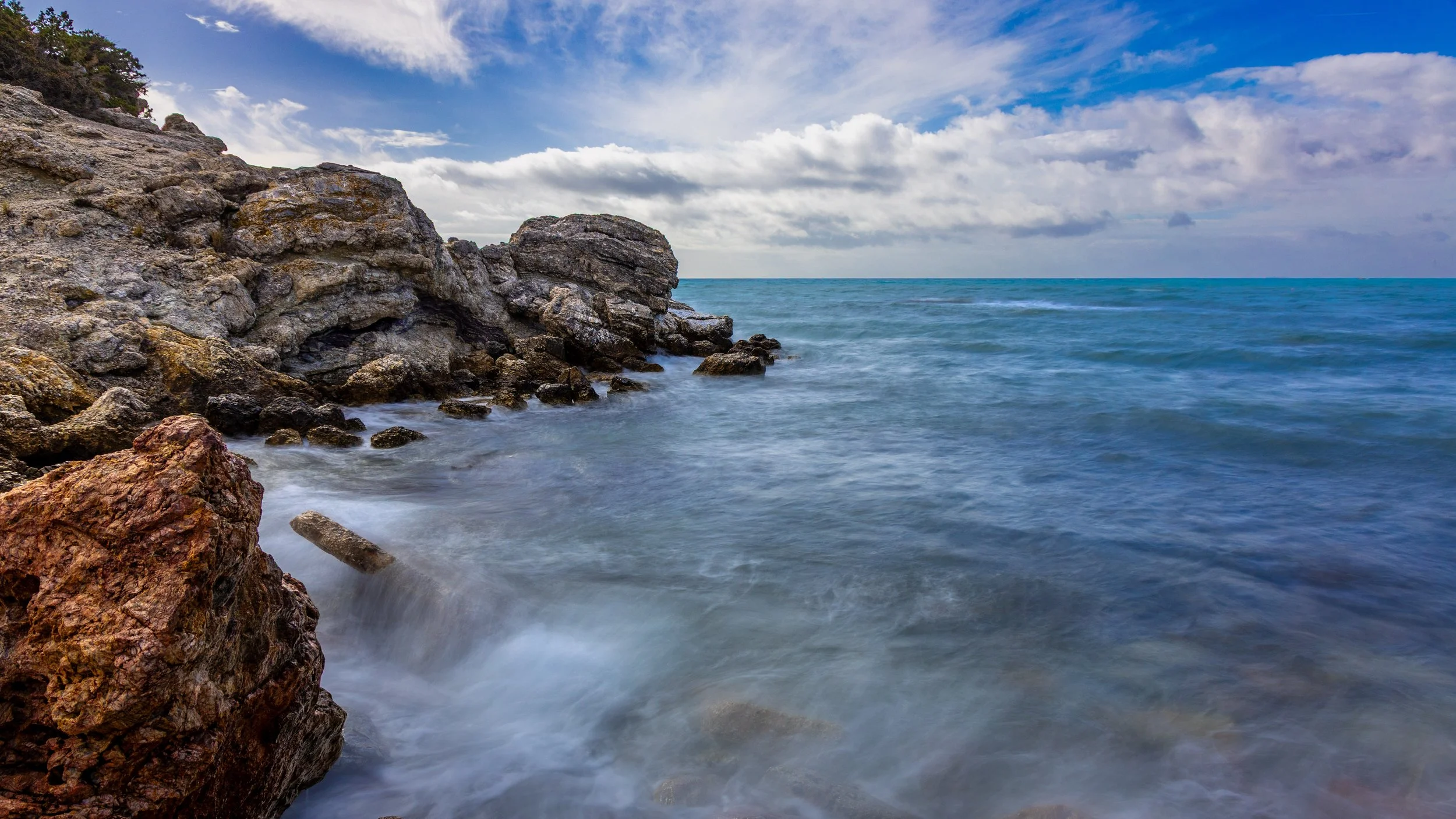 Ocean waves crashing against rocky shoreline under partly cloudy sky, photograph by erez nudmanov