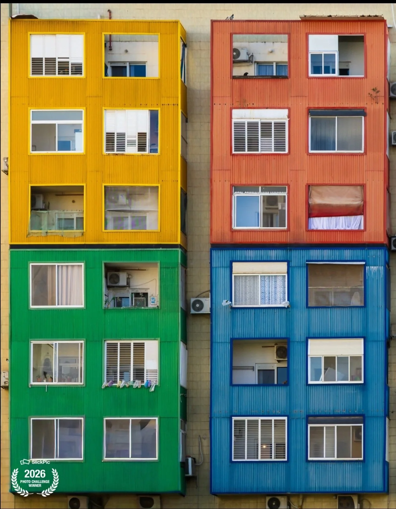 A colorful apartment building with yellow, orange, green, and blue sections, each with multiple windows.