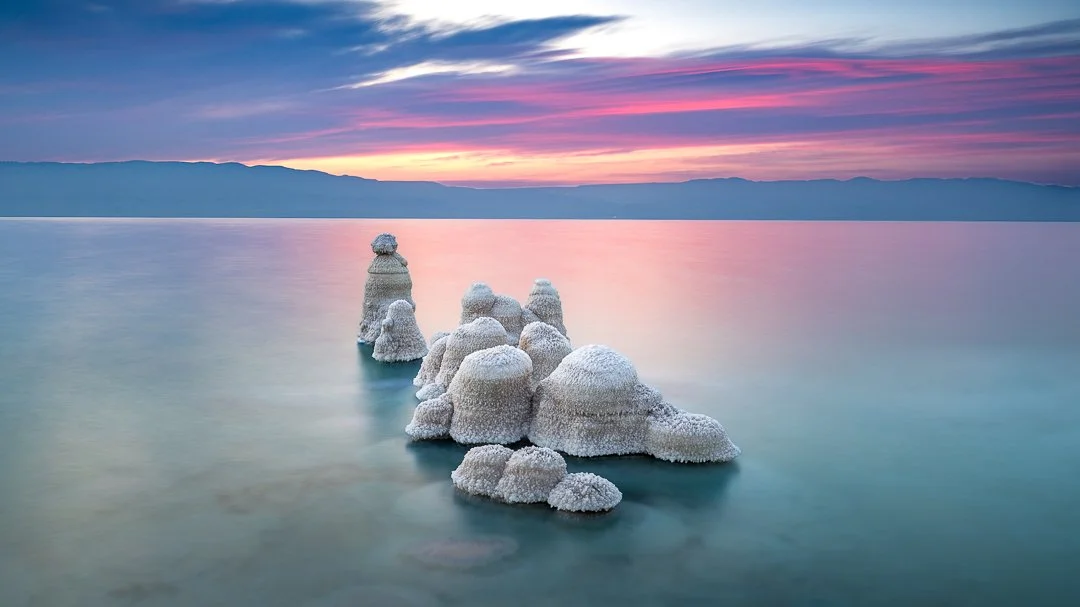 Salt formations rising from a calm lake during sunset with pink and purple hues in the sky.