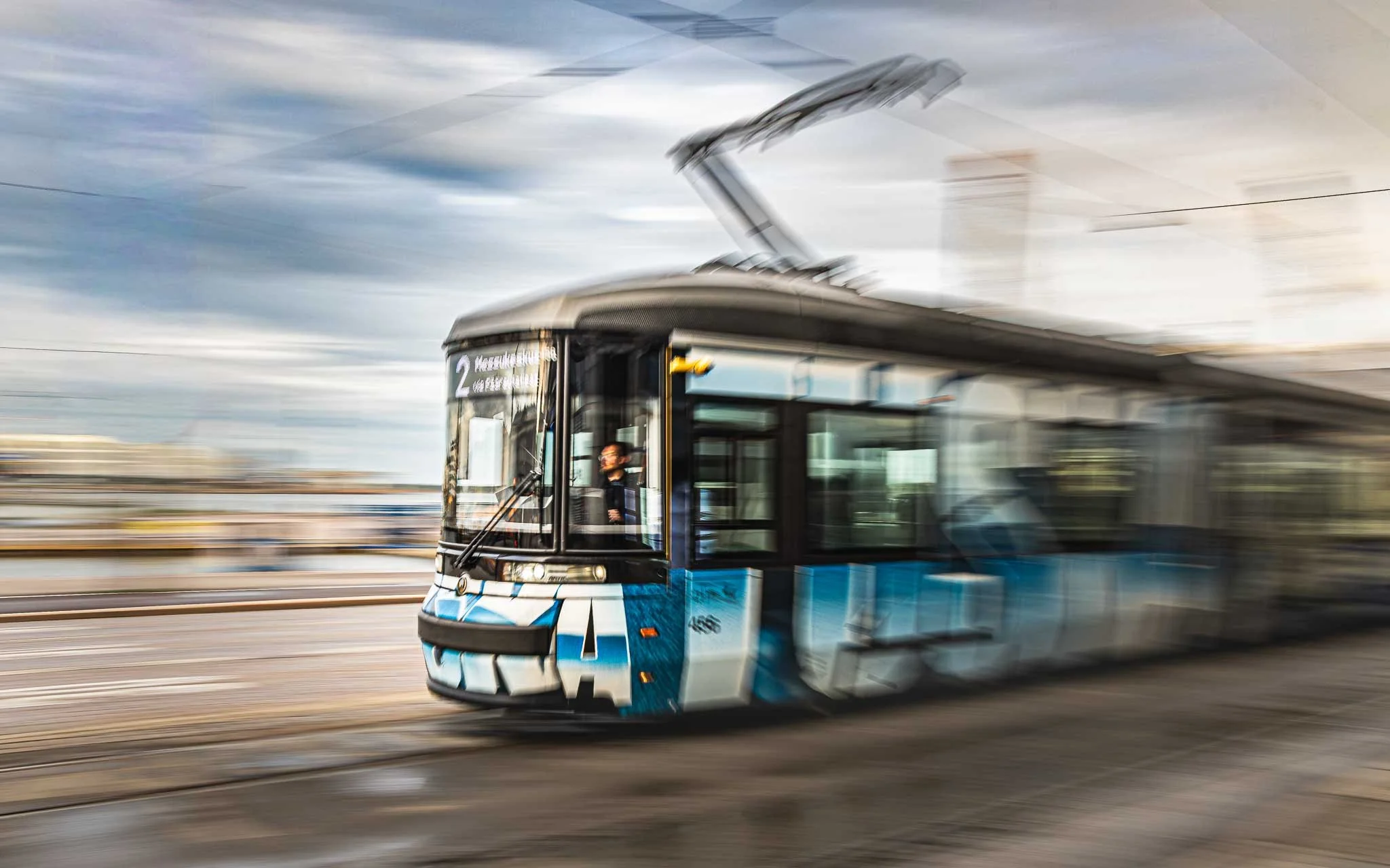 Blue tram in motion on an urban street, photographed with intentional motion blur and the driver visible through the front window.