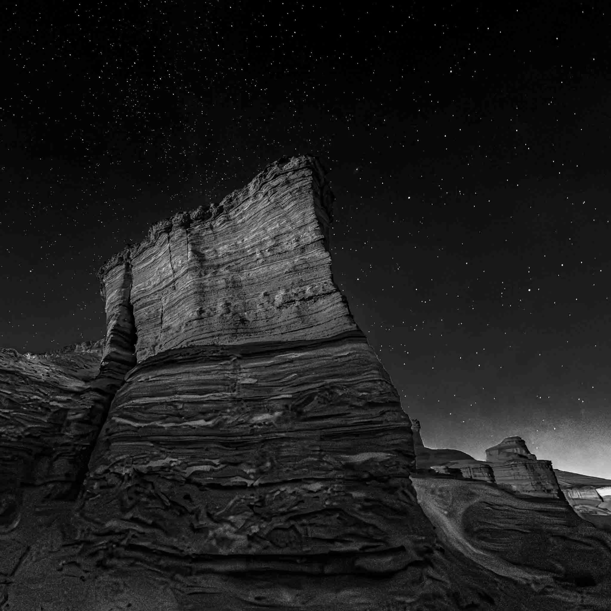 Black and white night landscape of the Havarei Masada formations beneath a star-filled sky near the Dead Sea.