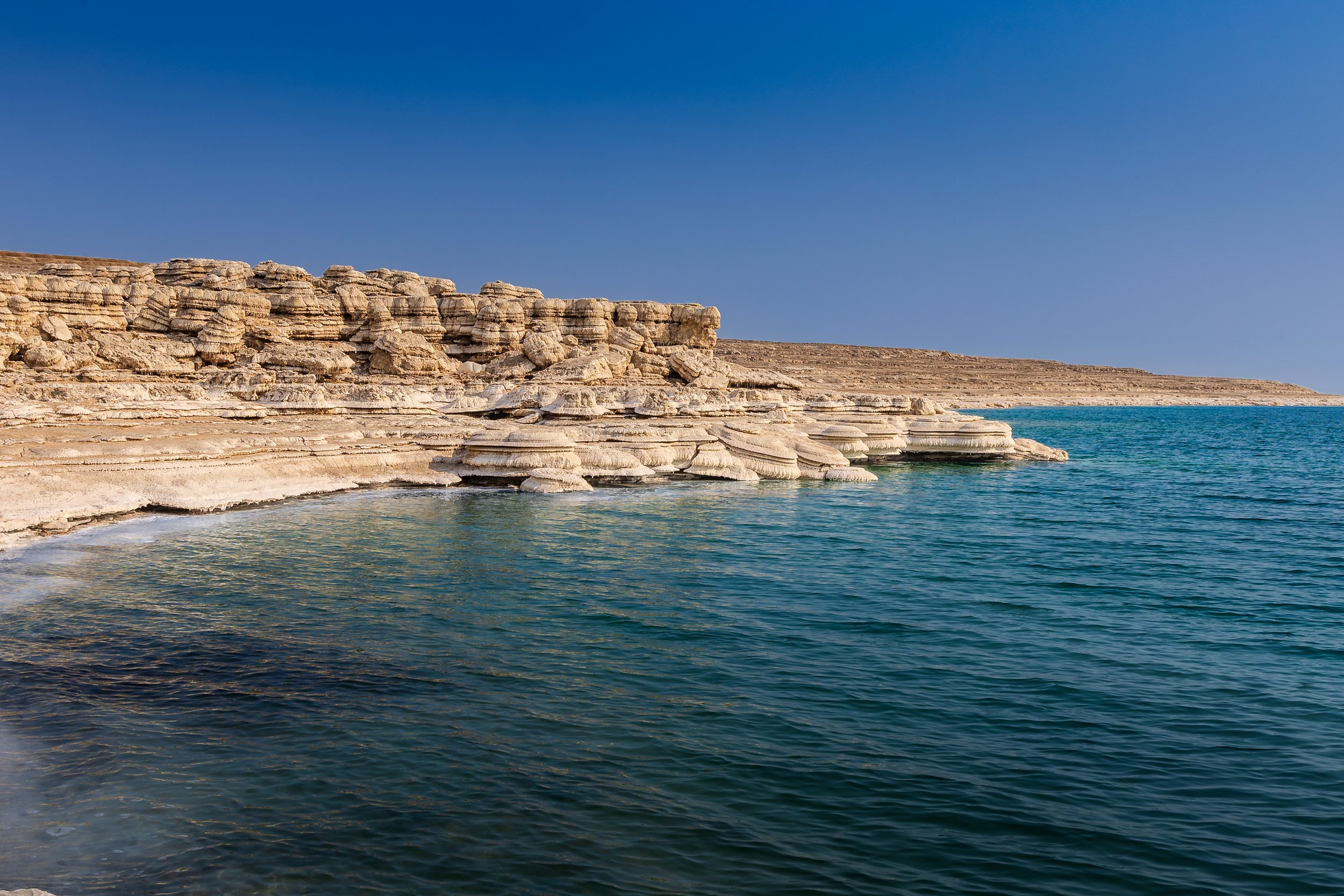 Scenic view of a rocky coastline with layered beige and white rocks meeting clear blue water under a bright blue sky.