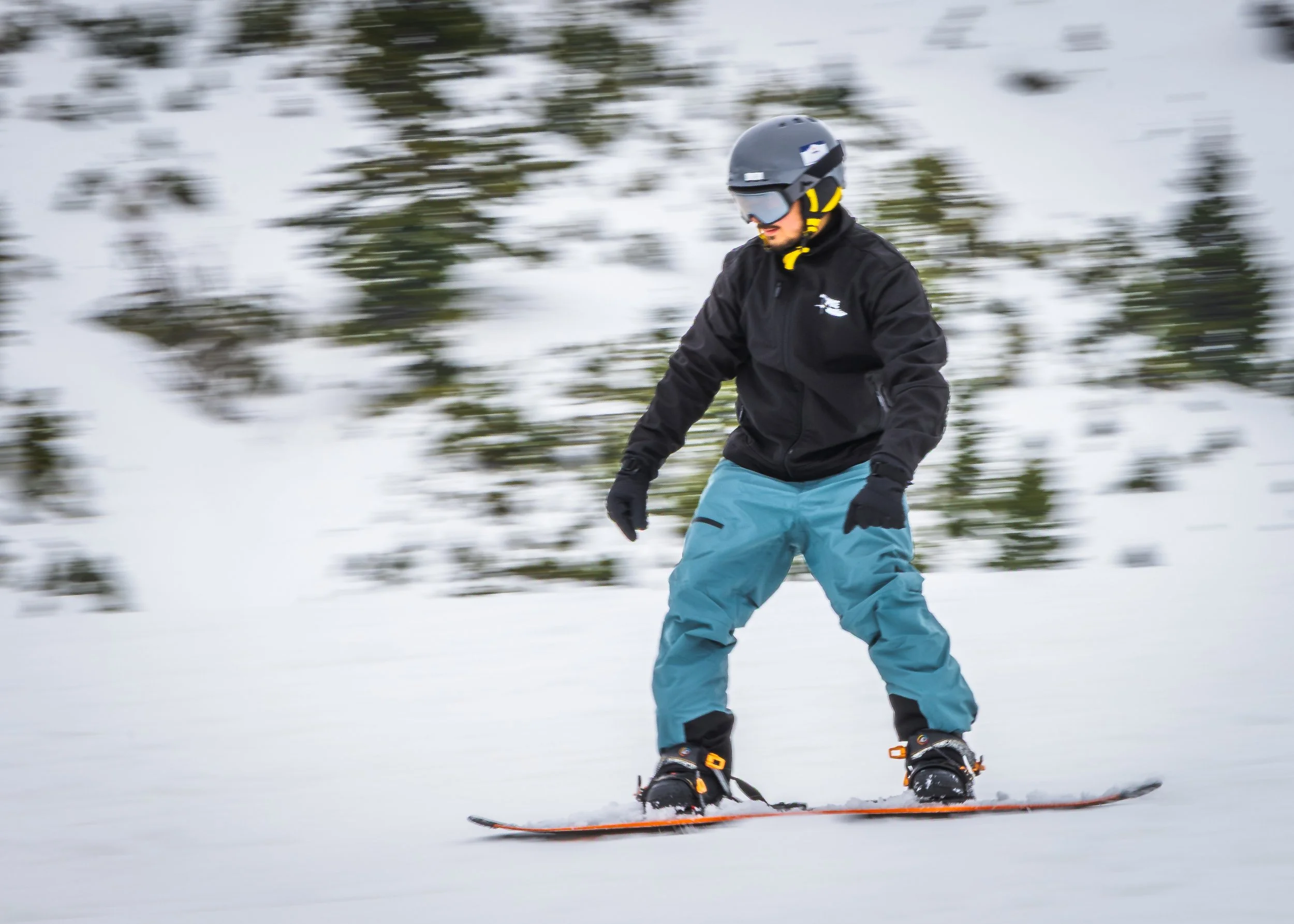 Person skiing on snow-covered slope wearing a black helmet and jacket, blue ski pants, and goggles in a wintry landscape photography by erez nudmanov