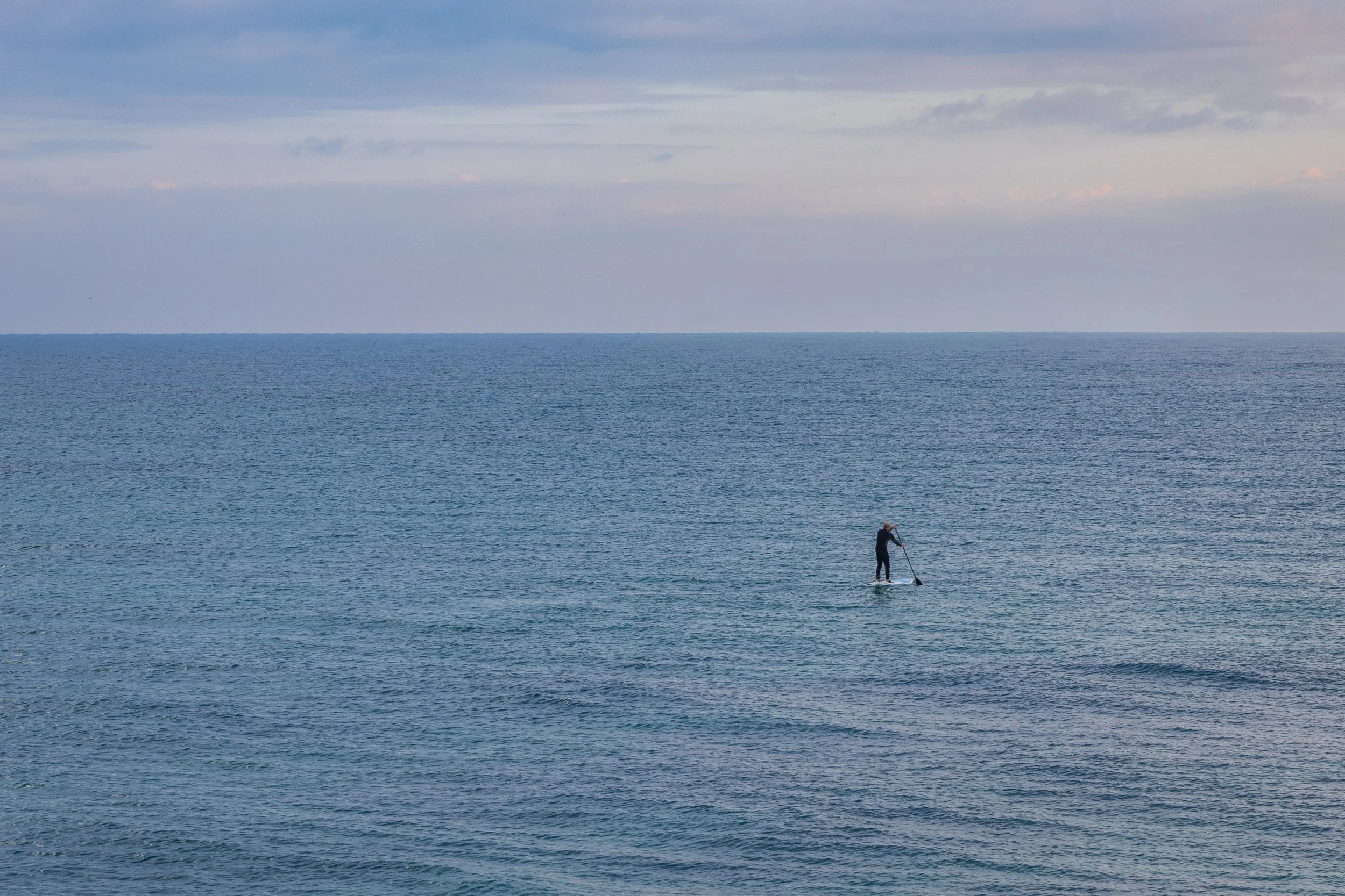 A person paddleboarding on calm ocean waters with a cloudy sky in the background.