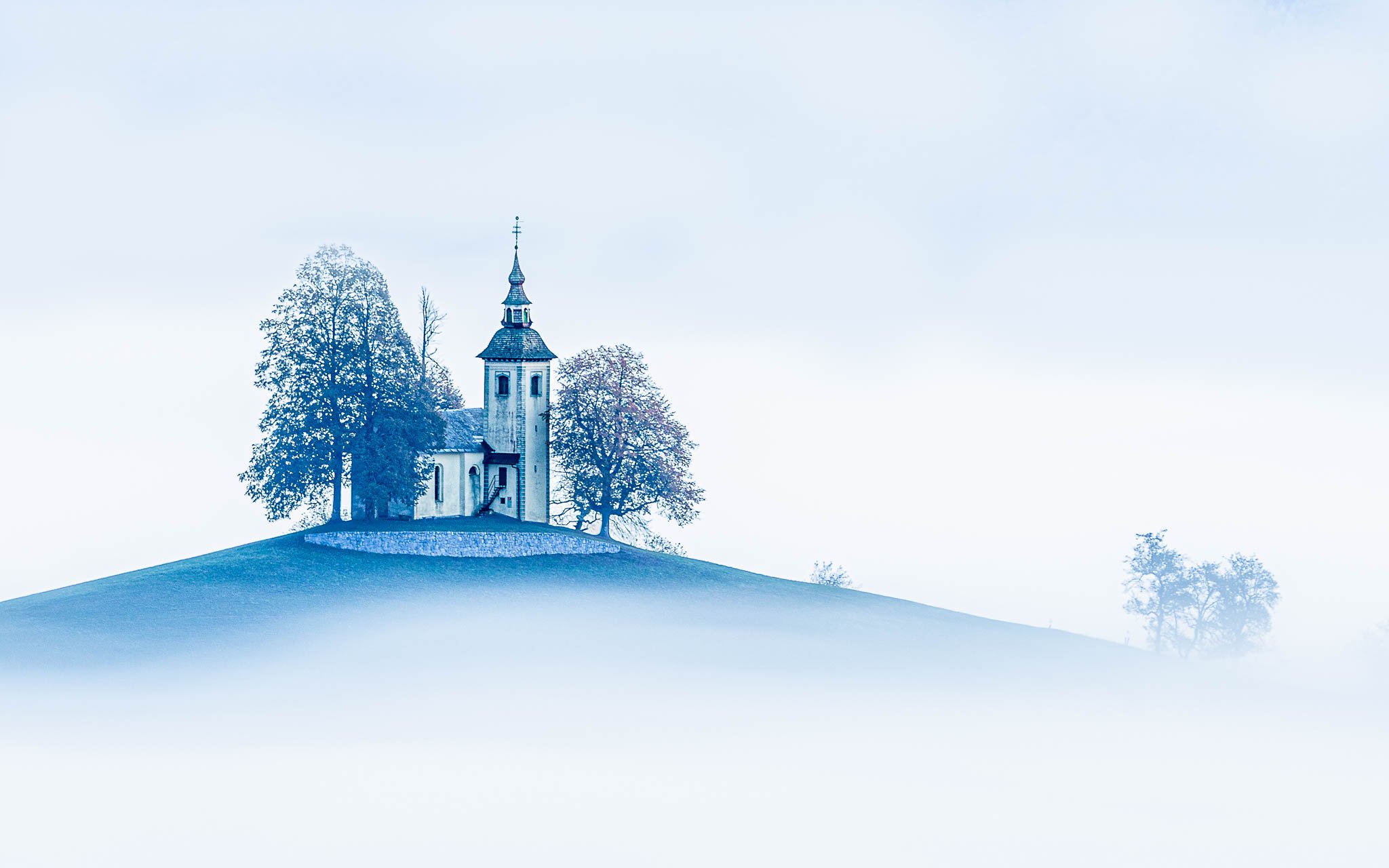 Church of St. Primož and Felicijan on a solitary hill surrounded by morning fog in Jamnik, Slovenia.