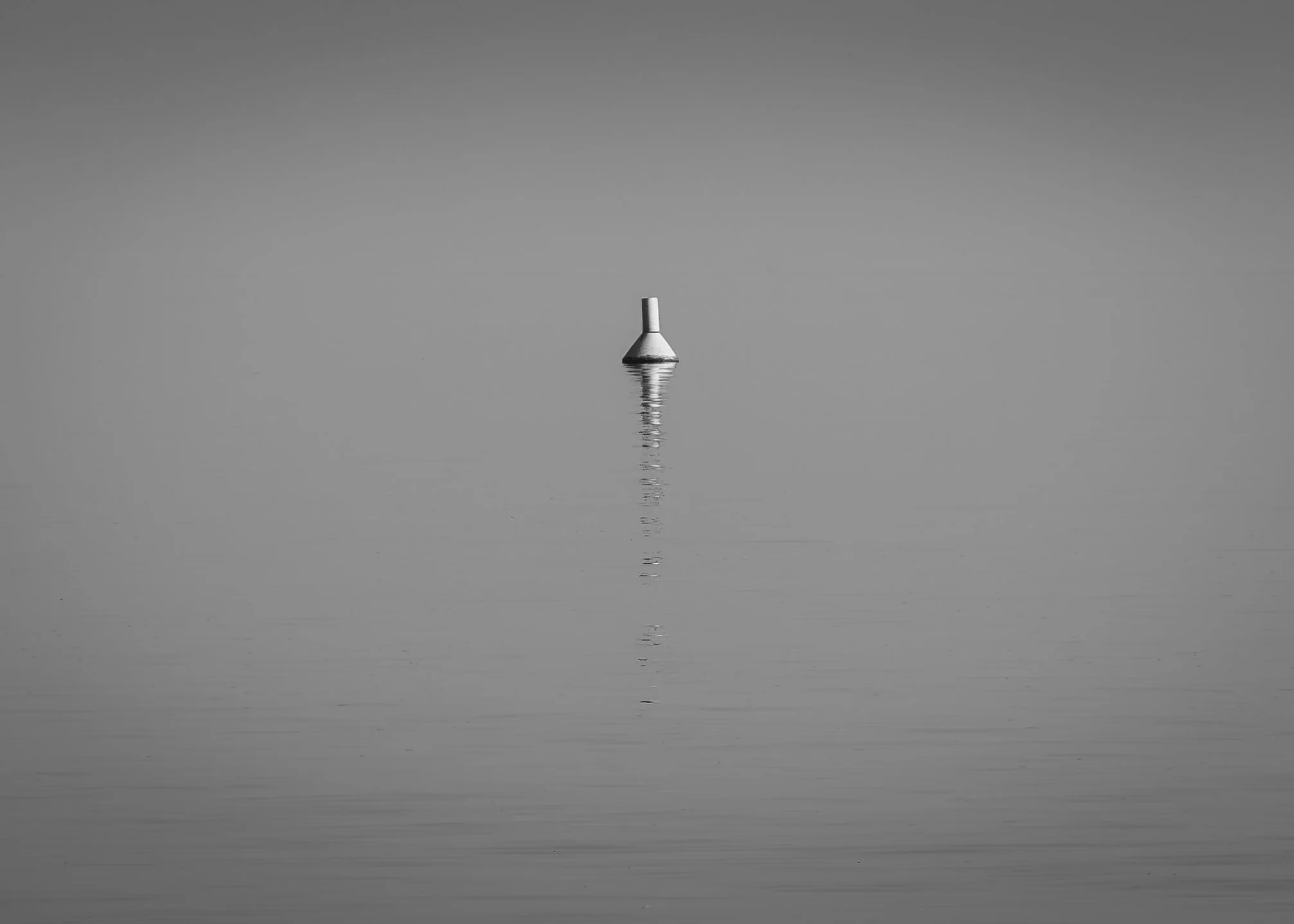 A lighthouse on calm water, with its reflection visible, under a clear sky, all in black and white photography by erez nudmanov