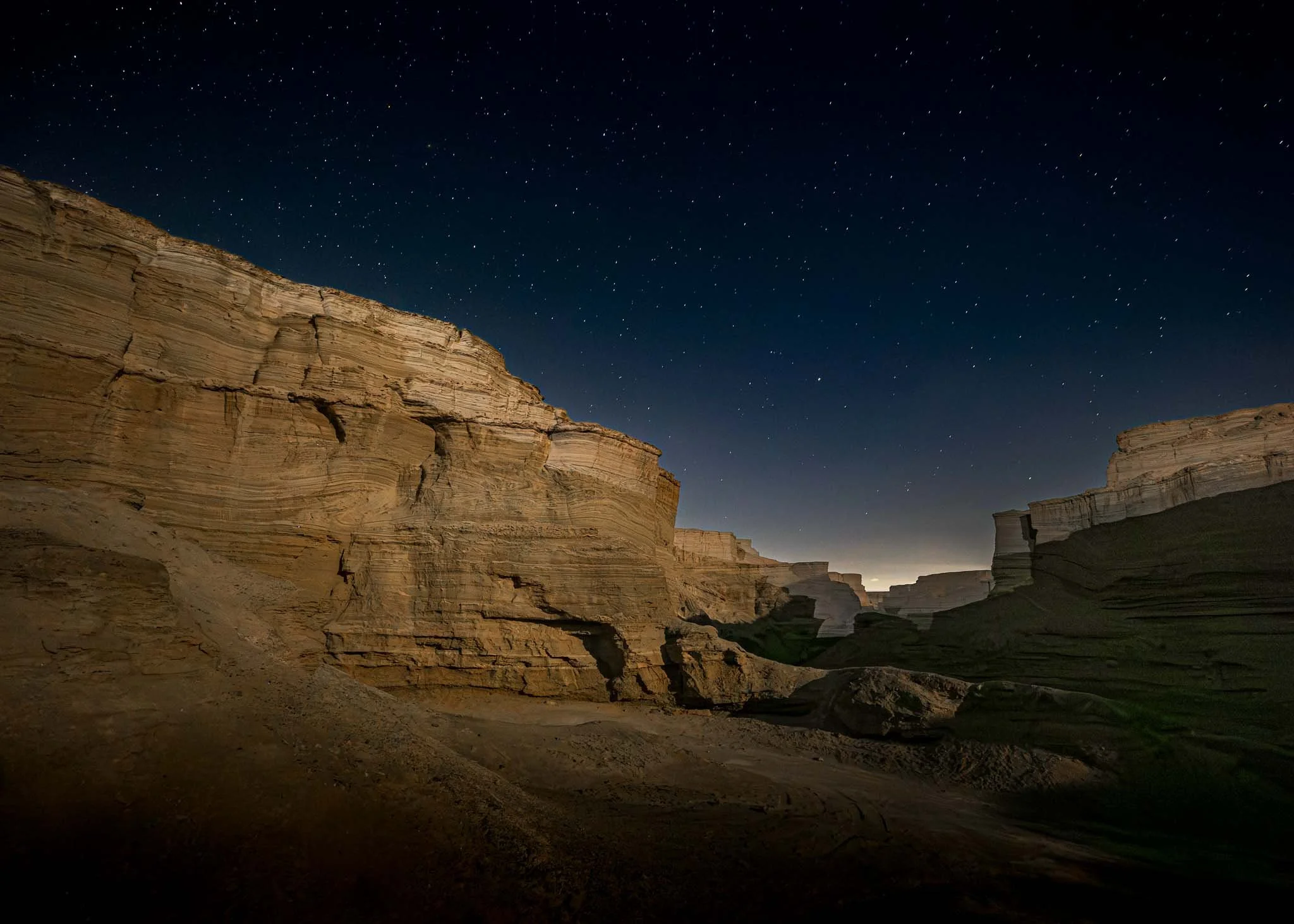 Night landscape of the Havarei Masada formations in Israel, illuminated beneath a star-filled desert sky near the Dead Sea.