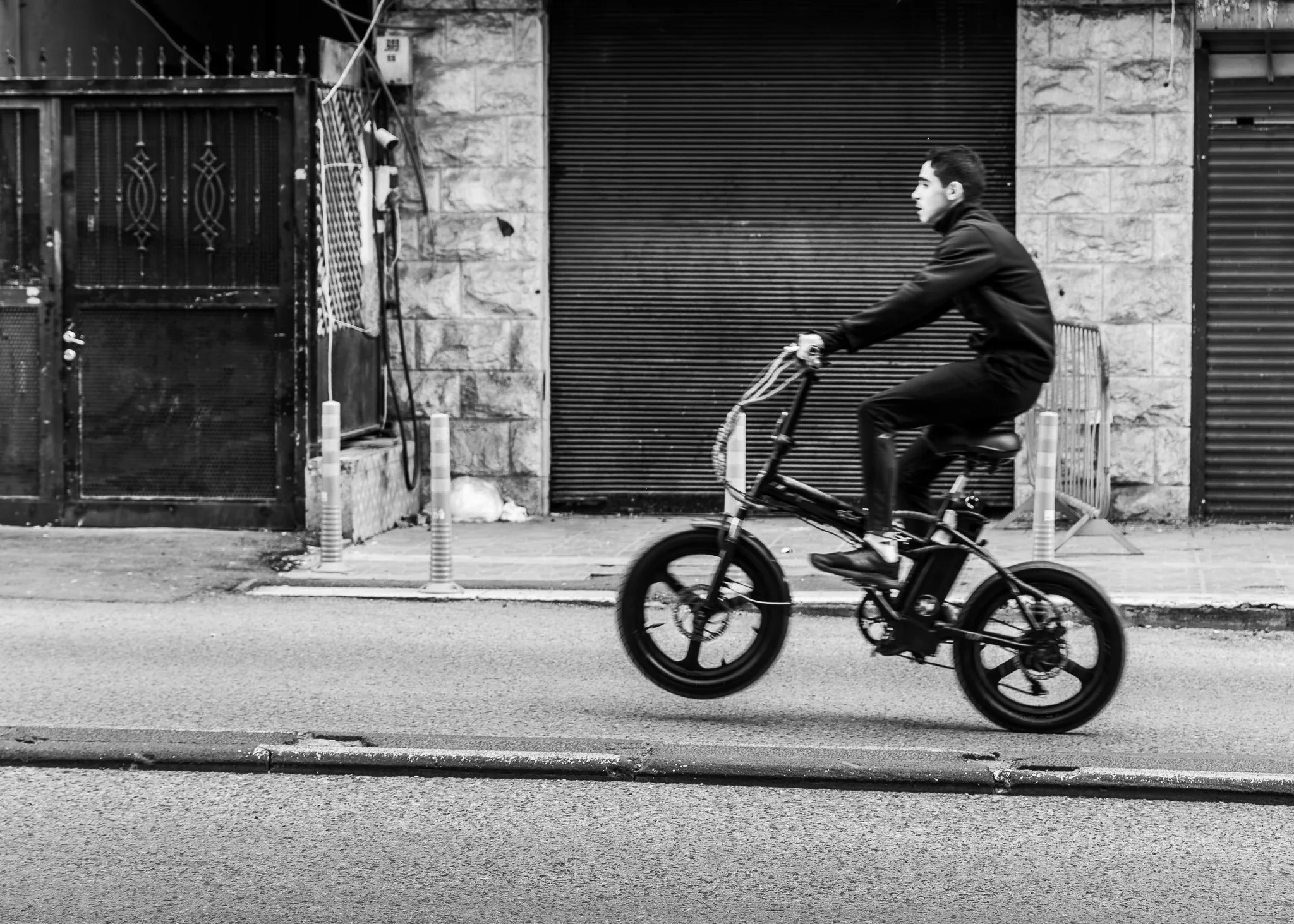 A man riding an electric bicycle on a city street in black and white.