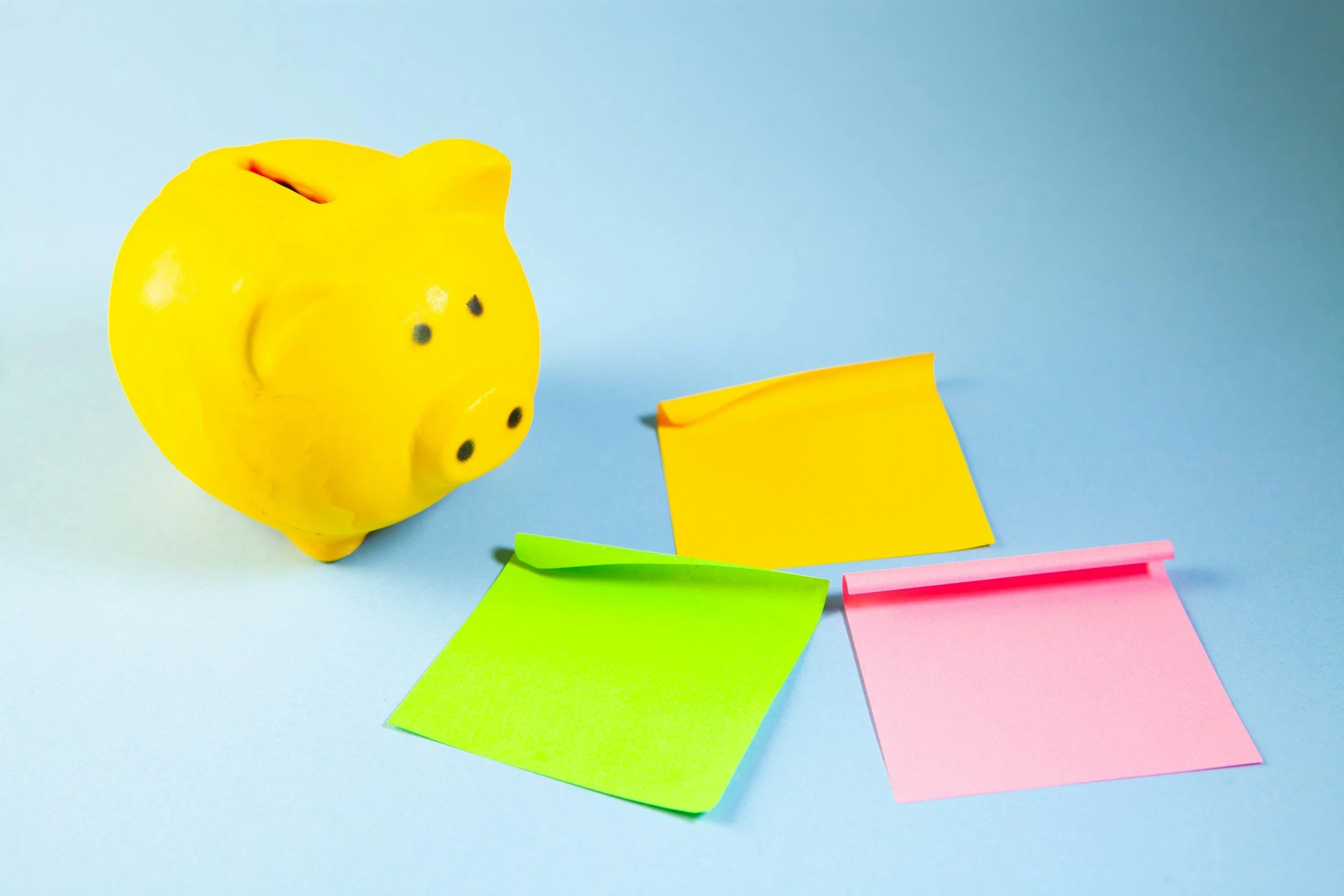 A piggy bank and three colored sticky notes.