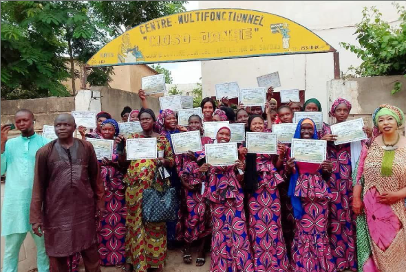 A group picture with many holding their school's diploma.