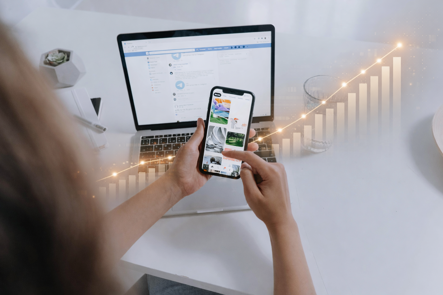 Person holding a smartphone with social media app, in front of a laptop and a glass of water, on a white desk with a small potted plant, and visual graphics of a rising bar chart overlayed.