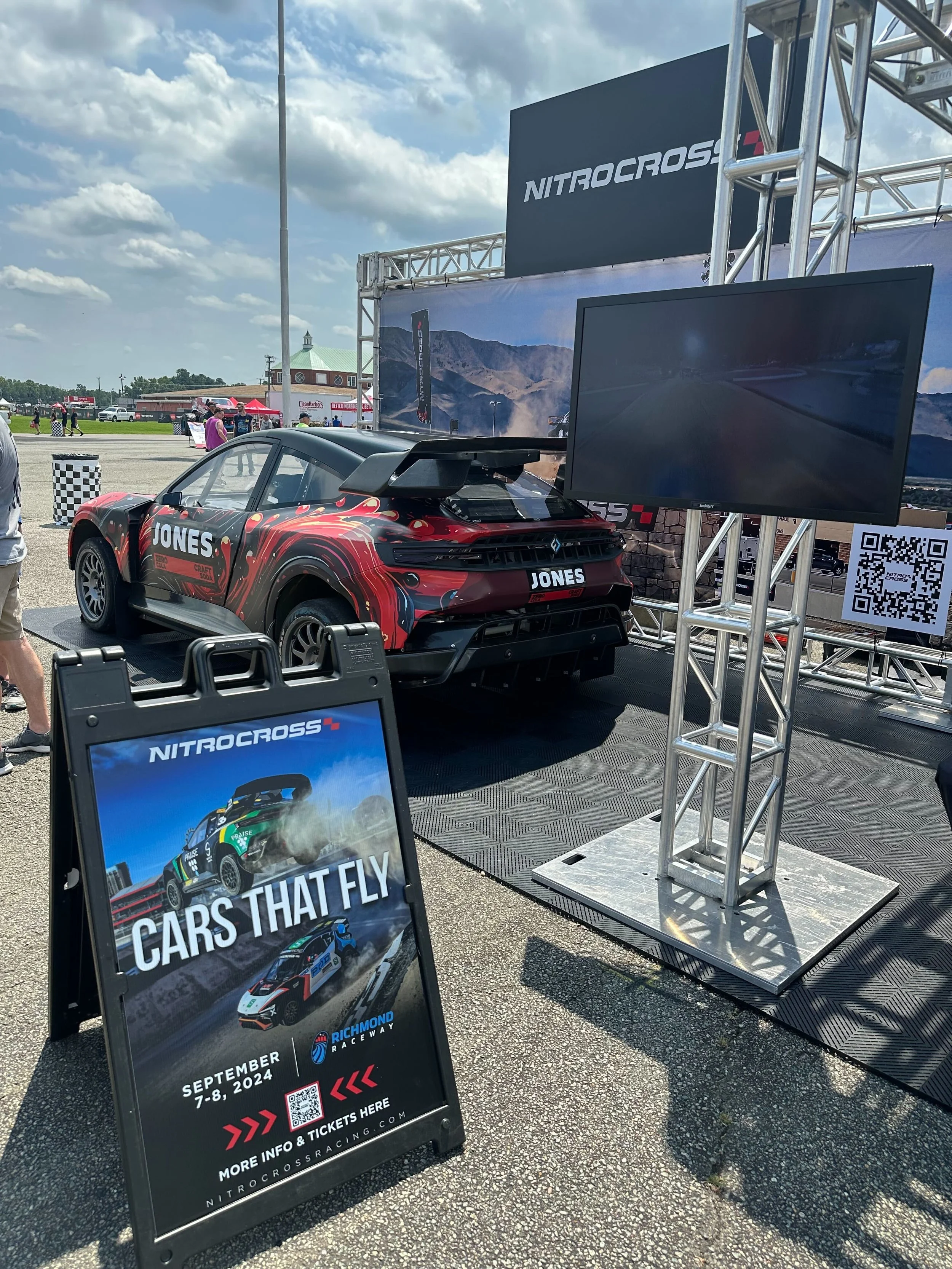 A race car on display at an outdoor event with a NitroCross banner and a sign advertising the event scheduled for September 7-8, 2024 at Richmond Raceway.