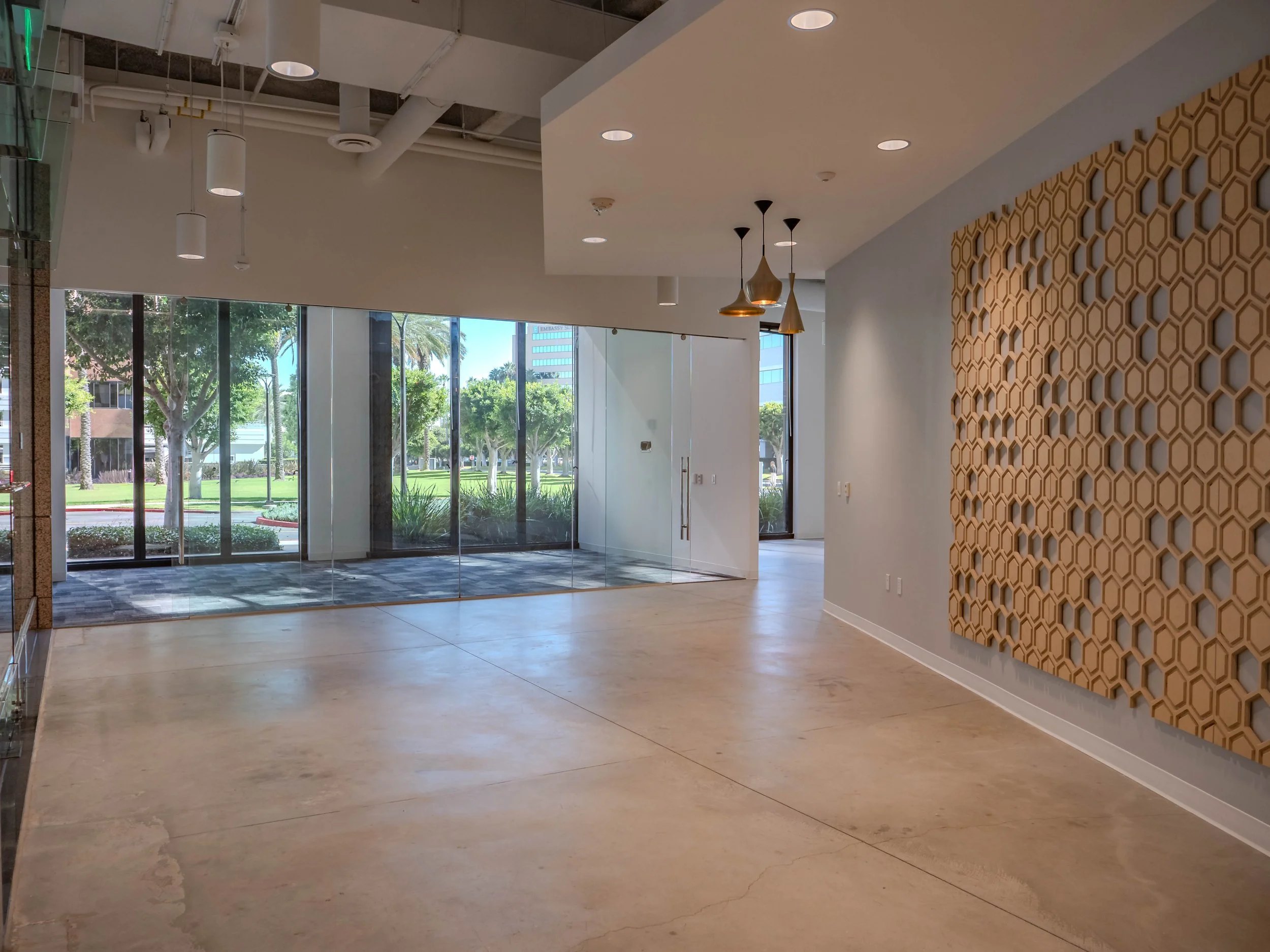 Empty modern lobby with large glass windows, honeycomb wall decoration, pendant lighting, and polished concrete floors.