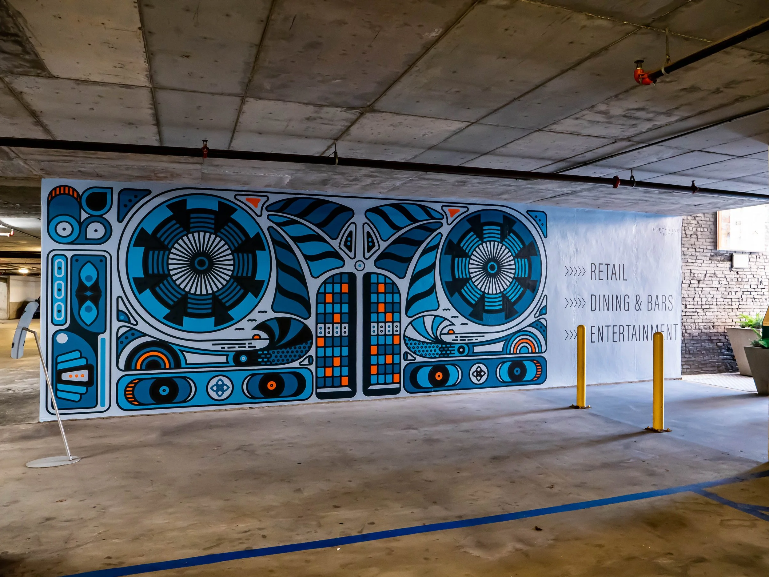 Colorful street art mural featuring abstract geometric shapes and patterns, with a part of the wall displaying text listing retail, dining & bars, and entertainment, located in a parking garage.