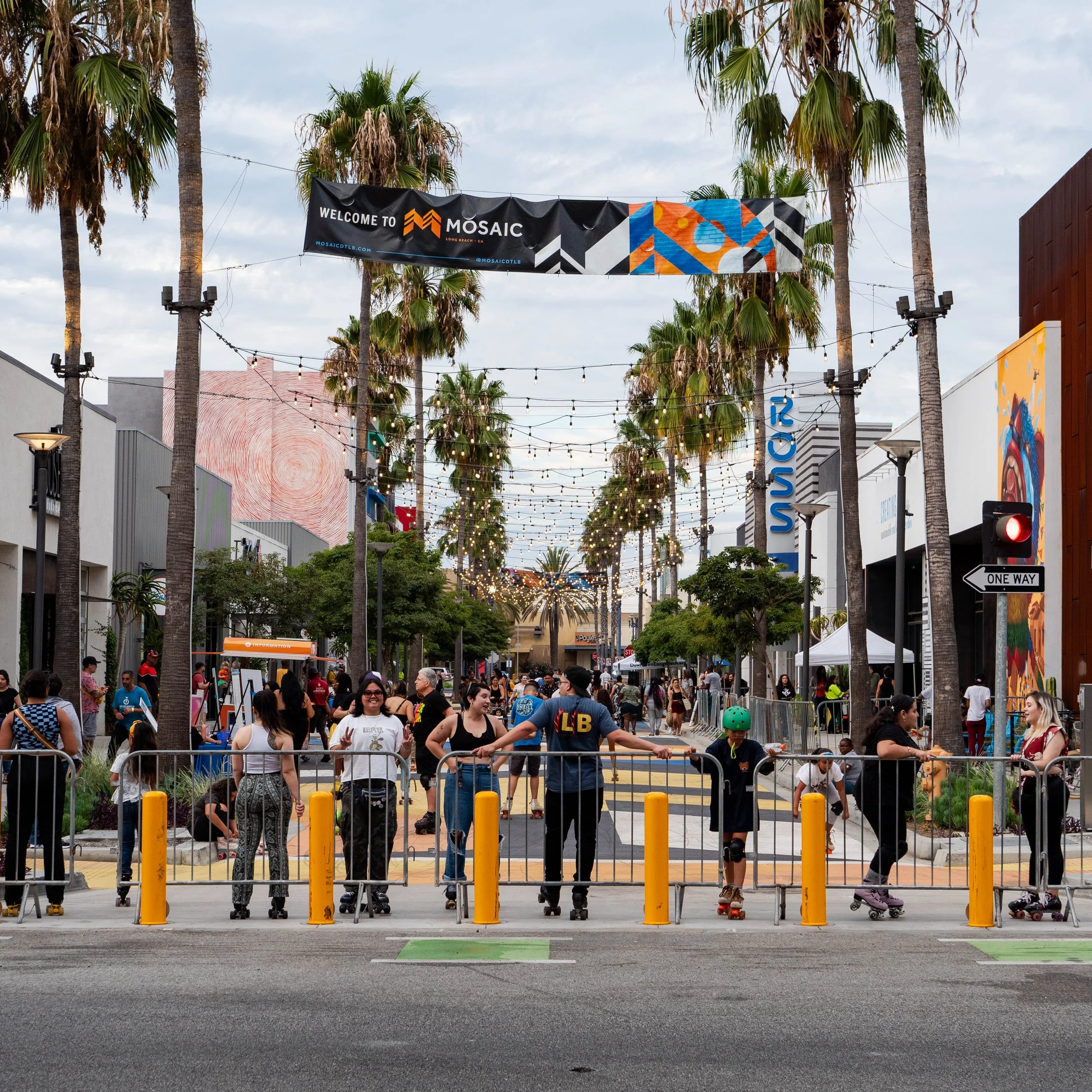 People roller skating on a closed-off street during an outdoor event with string lights and palm trees, at MOSAIC shopping center.