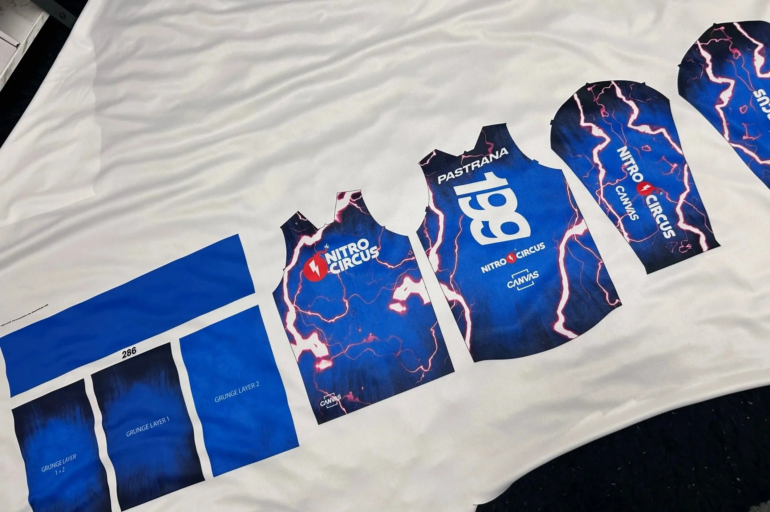 Designs for BMX racing jerseys laid out on fabric, showing Lightning bolt patterns, the Nitro Circus logo, and text including 'Pastrana,' '199,' and 'Canvas'.