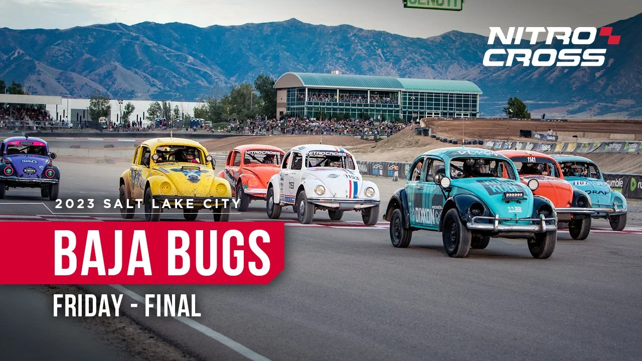 Cars participating in a vintage car race at Salt Lake City, with mountains in the background, spectators in the stands, and event branding for Nitro Cross and Baja Bugs.