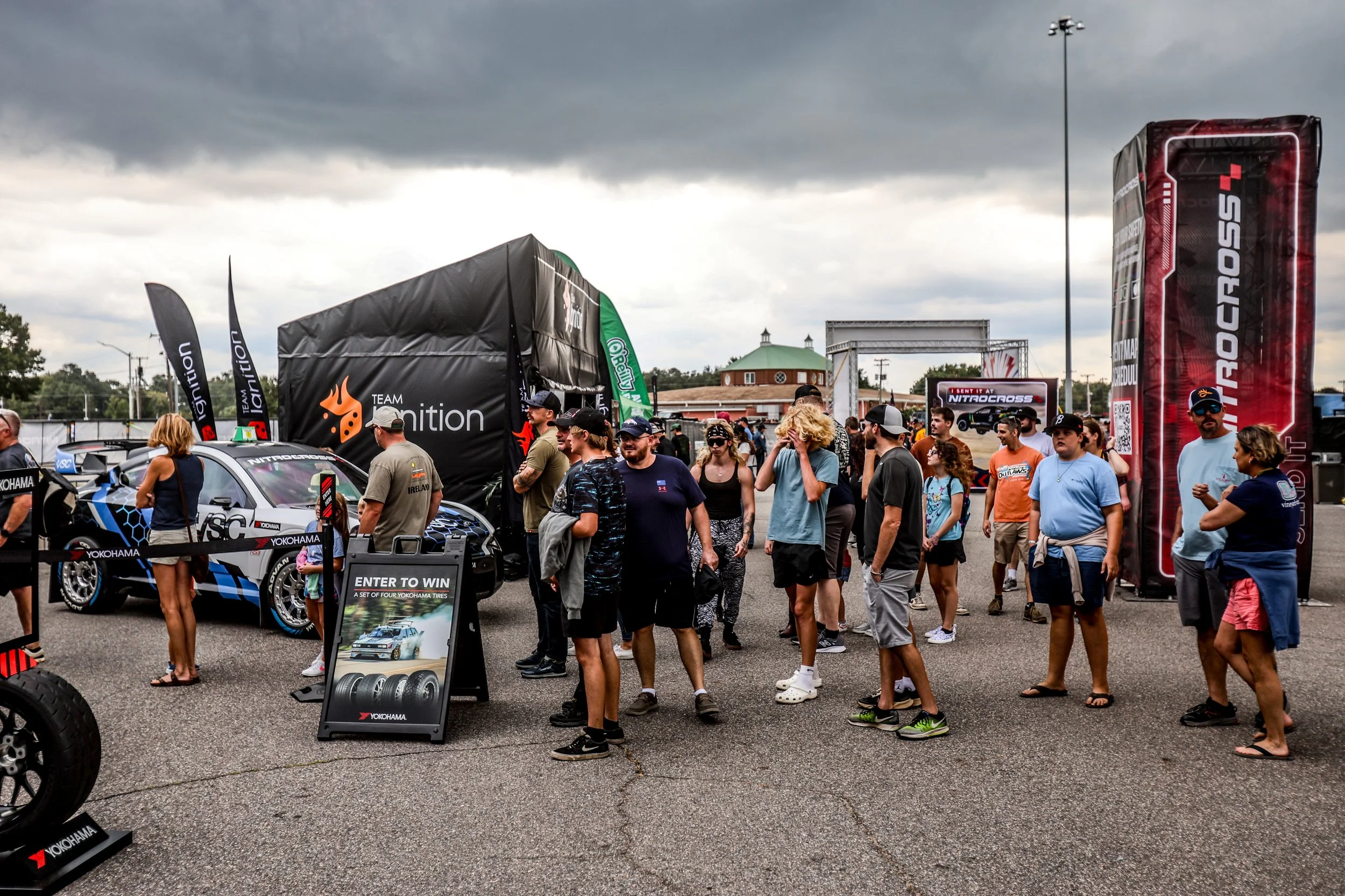 People gather at a car exhibition with a race car and promotional banners.