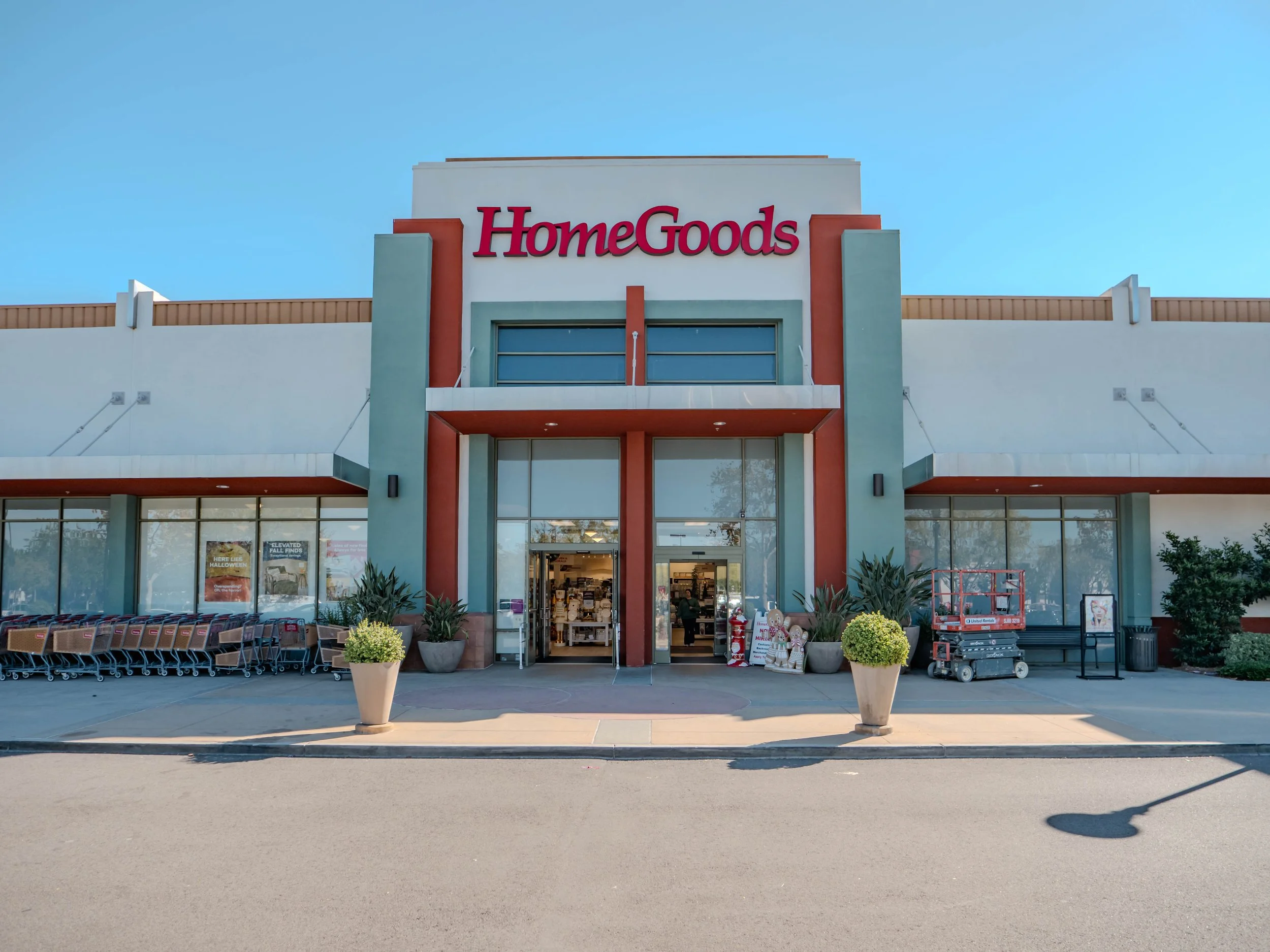 Front view of a HomeGoods store with large windows, entrance doors, shopping carts, and potted plants outside, under a clear sky.