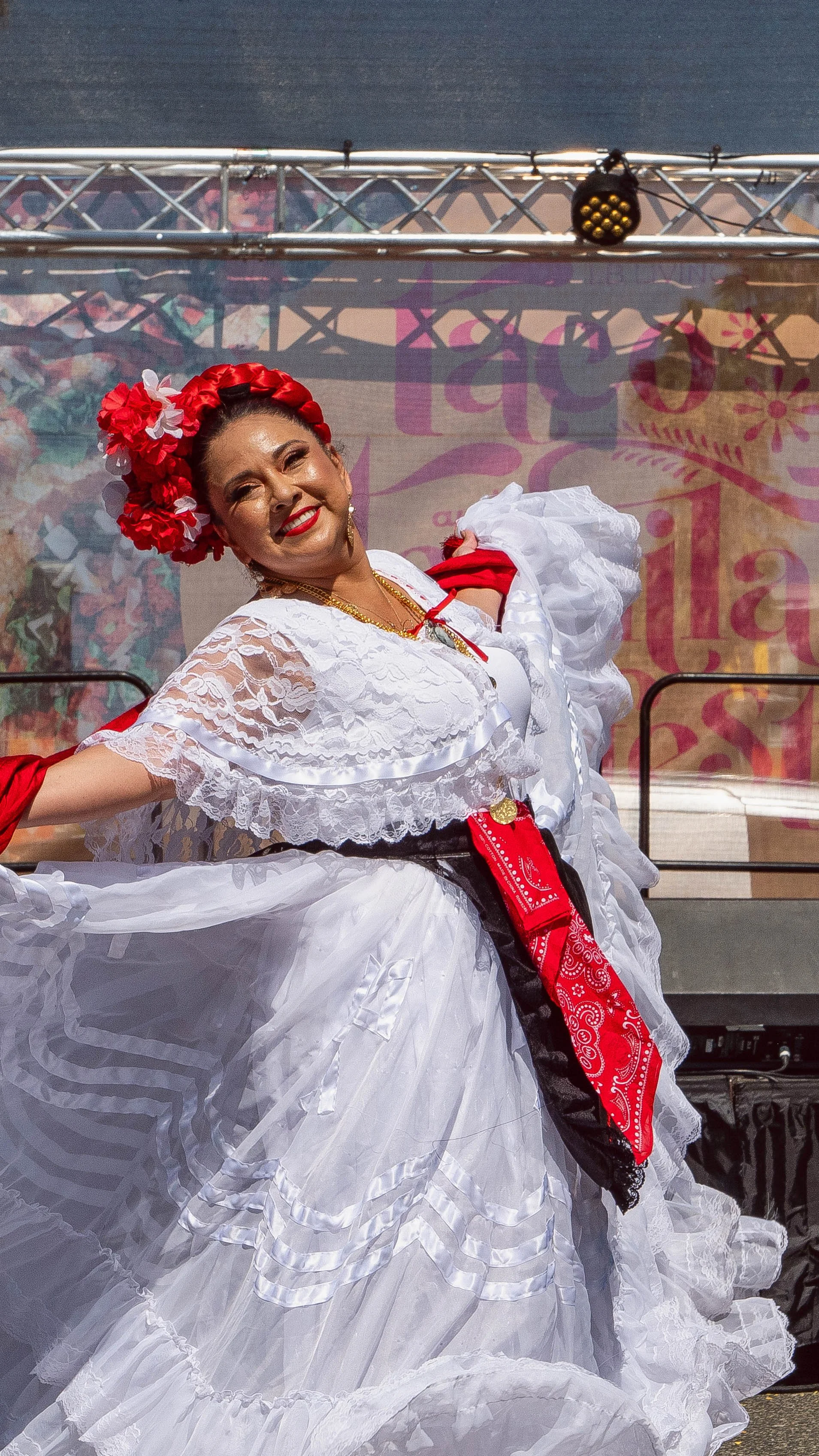 Woman dressed in traditional Mexican folkloric dress, dancing with a big smile at a cultural festival.