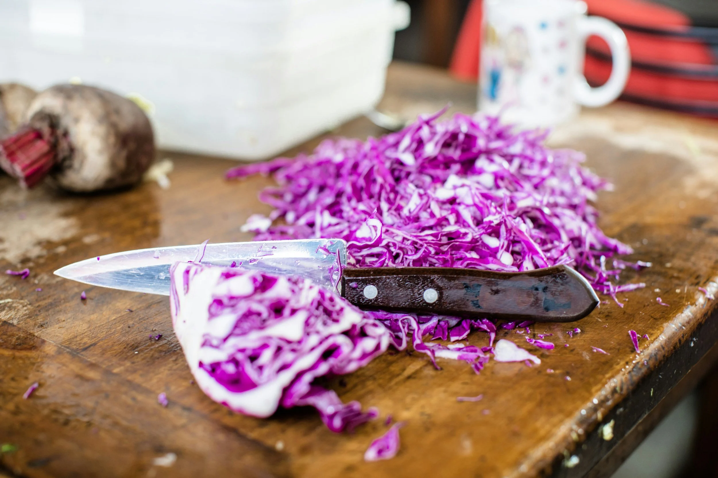 Shredded purple cabbage on a wooden cutting board with a knife, and a partially sliced piece in the foreground.