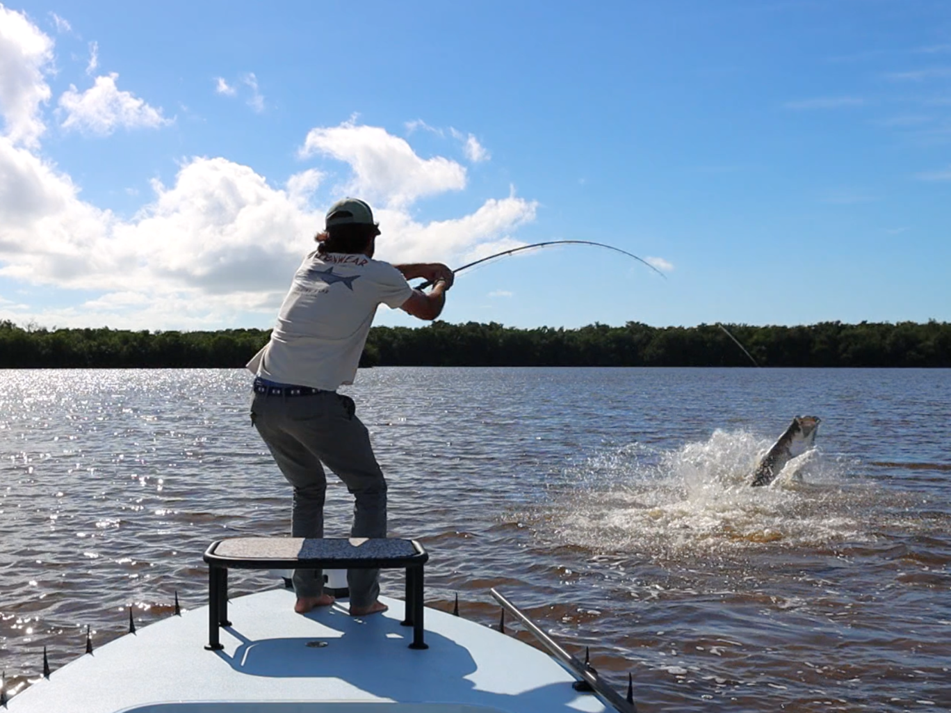 Person fishing from a boat on a body of water with a fish jumping out of the water.