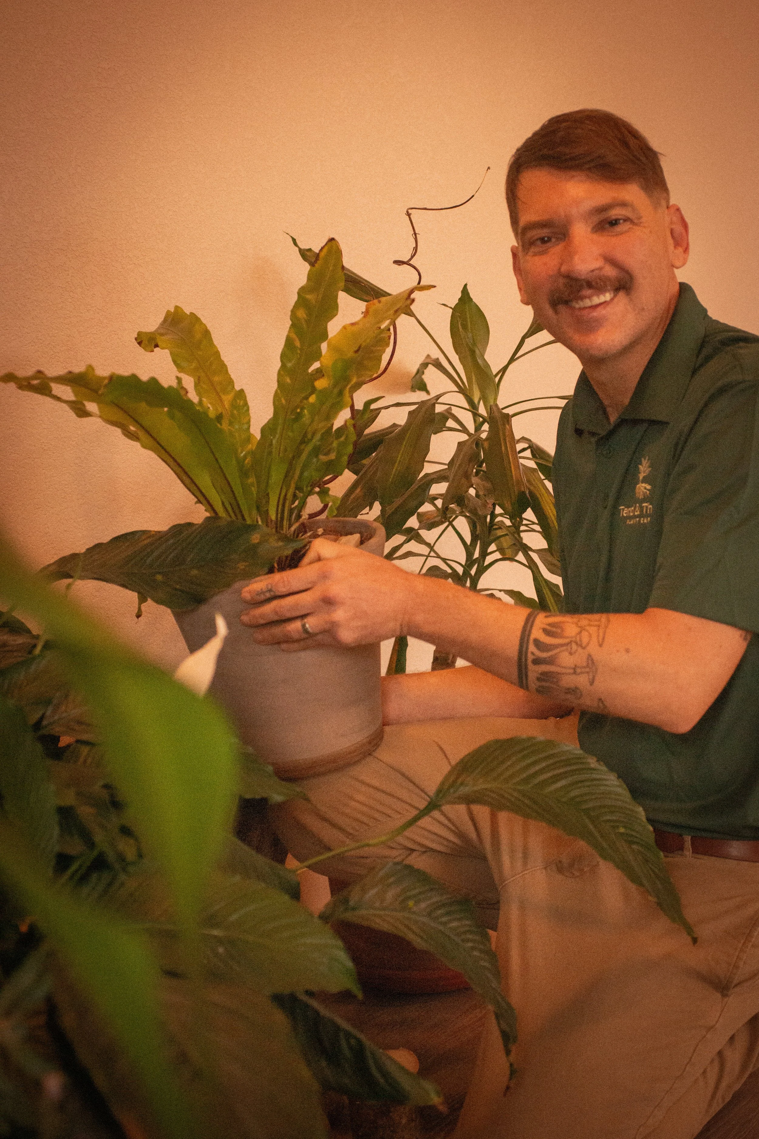 A man smiling while holding a potted plant indoors.